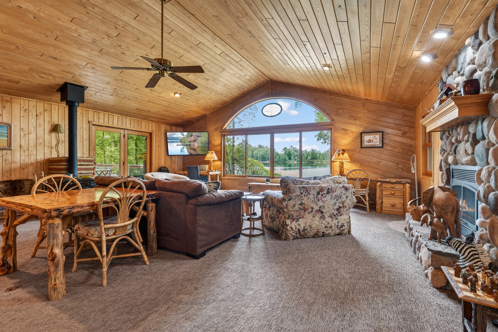 Relax in your warm, wood-paneled retreat with vaulted ceilings, stone fireplace, and stunning lakefront views. Gather around the rustic dining table or unwind by the cozy fire.