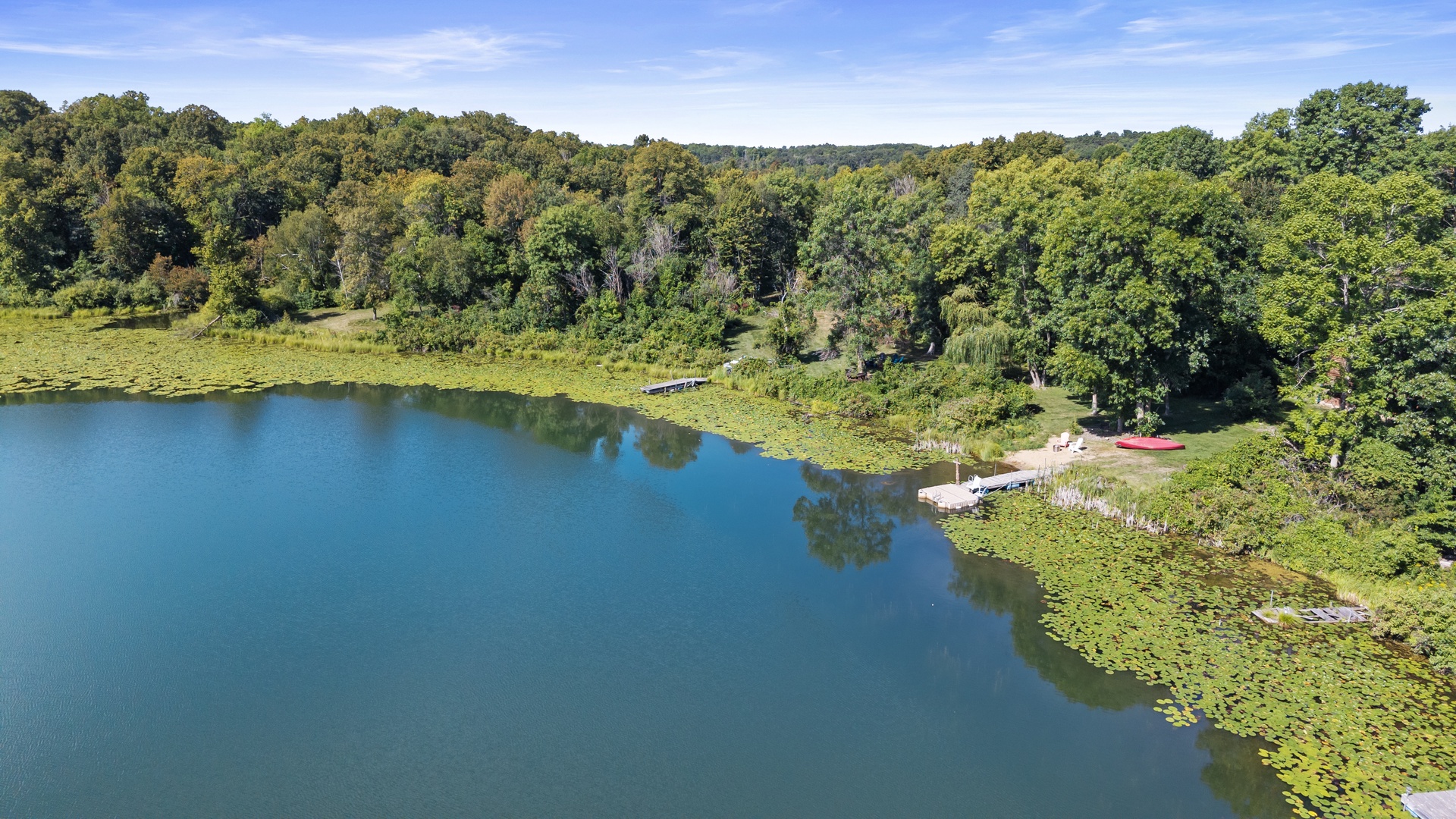 An aerial perspective of the property reveals a private lake dock and waterfront access bordered by mature forest and rolling hillsides, offering a secluded natural setting.