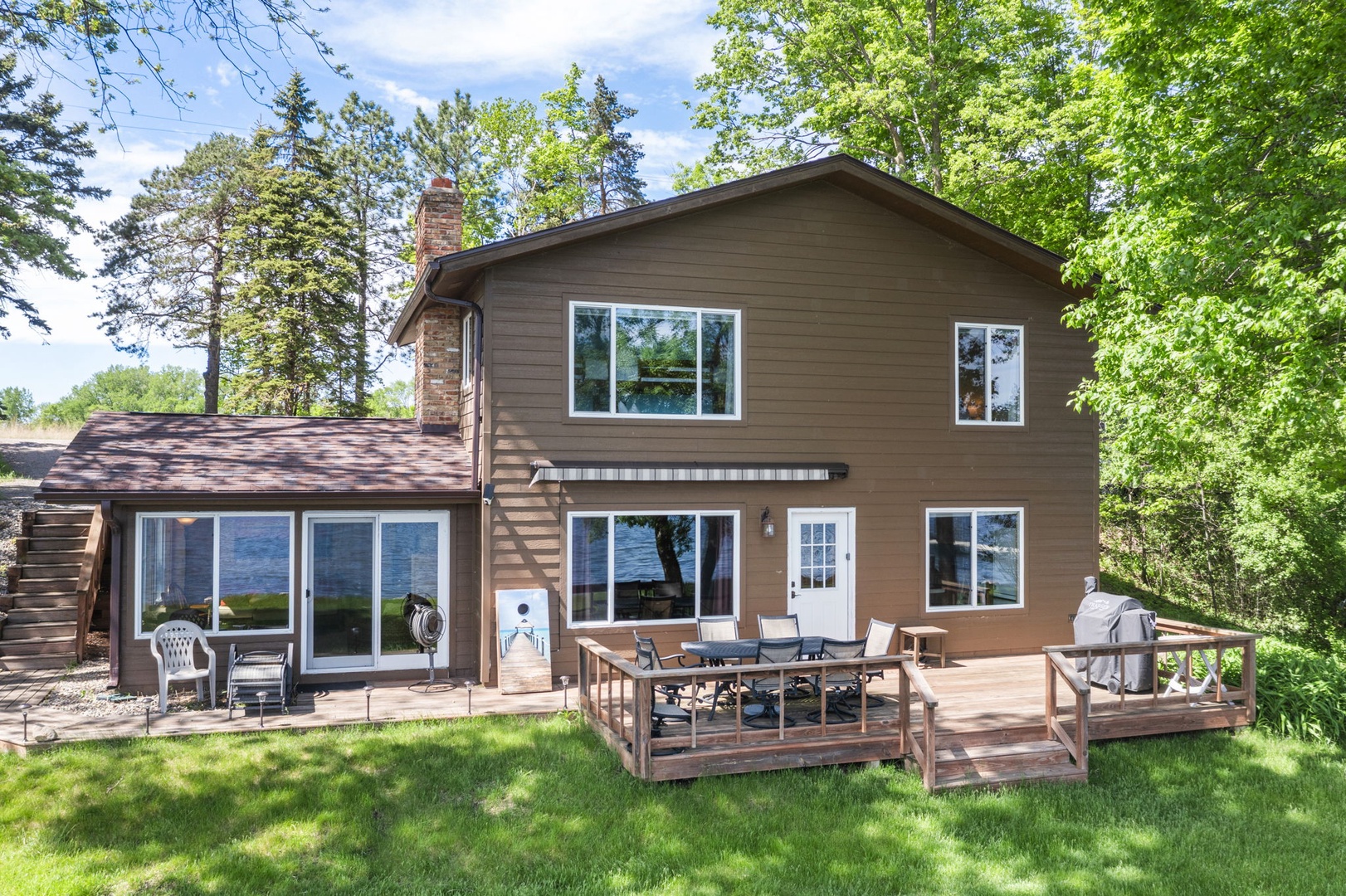 A spacious vacation home surrounded by lush greenery, featuring a welcoming deck area and large windows framing views of the natural landscape.