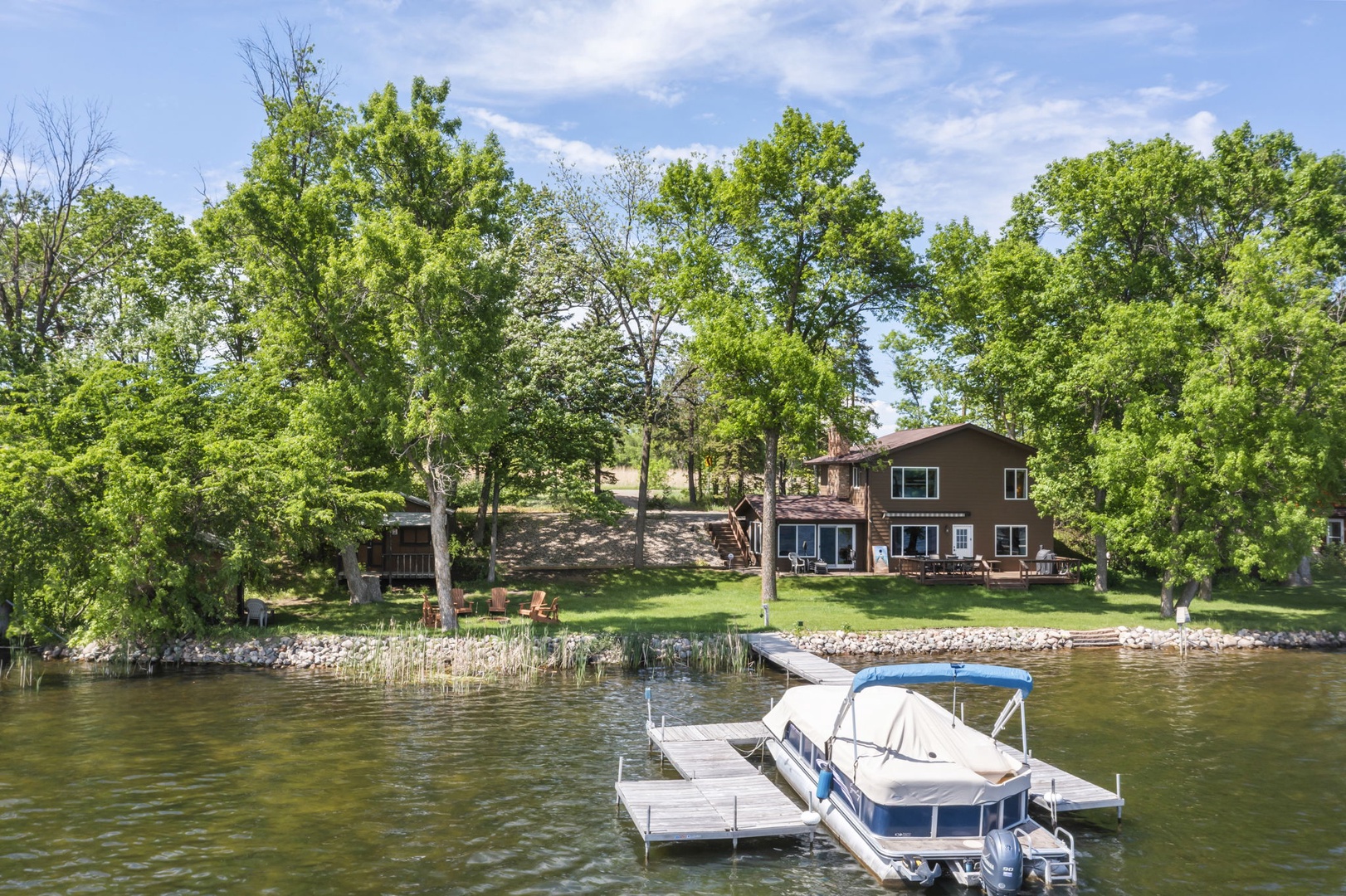 Lakefront property with private dock, surrounded by mature trees and lush green lawn, offering water access in a peaceful natural setting.