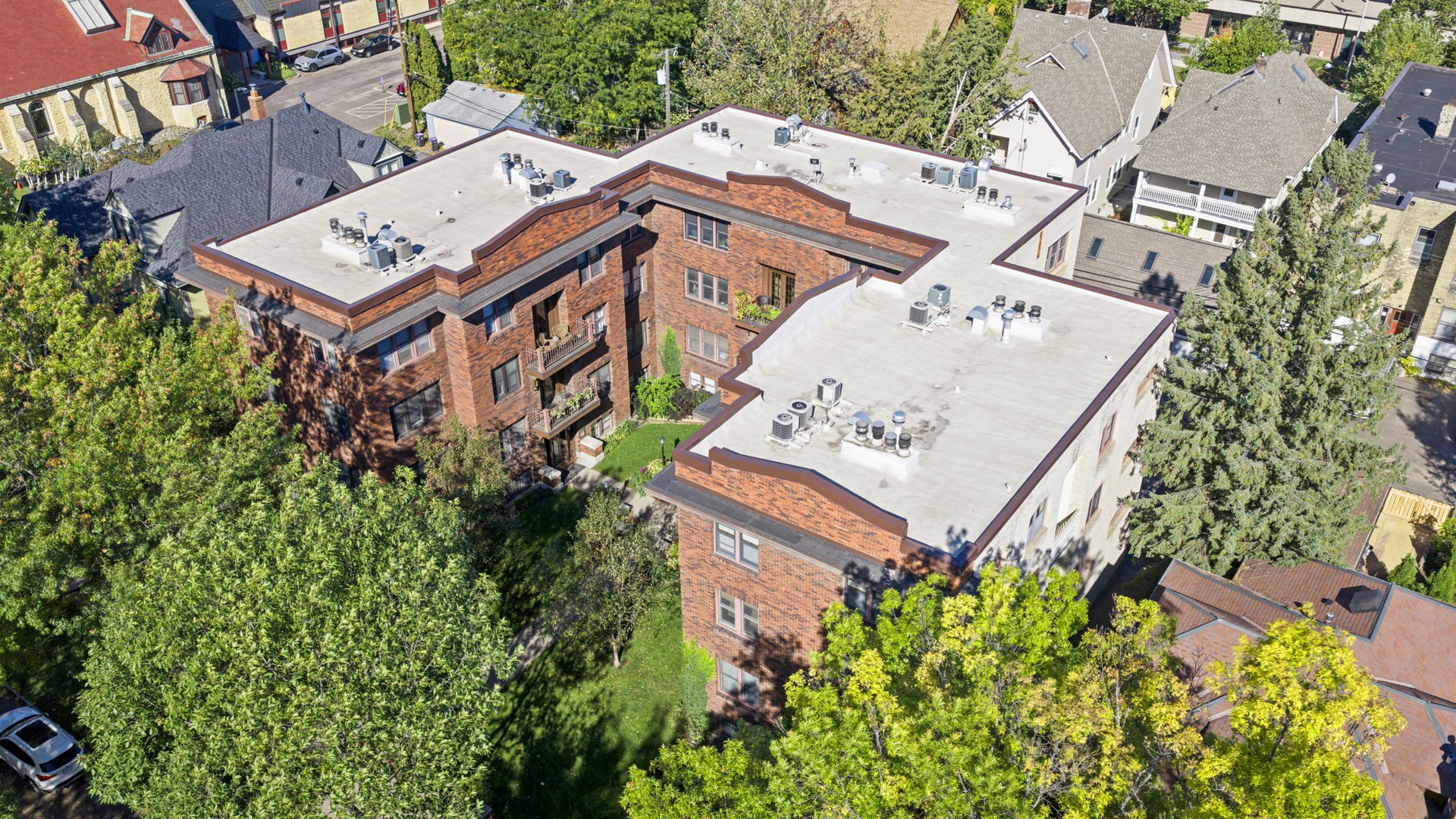 Aerial view of the property and its surrounding residential neighborhood, showcasing the red-brick building nestled among mature trees.