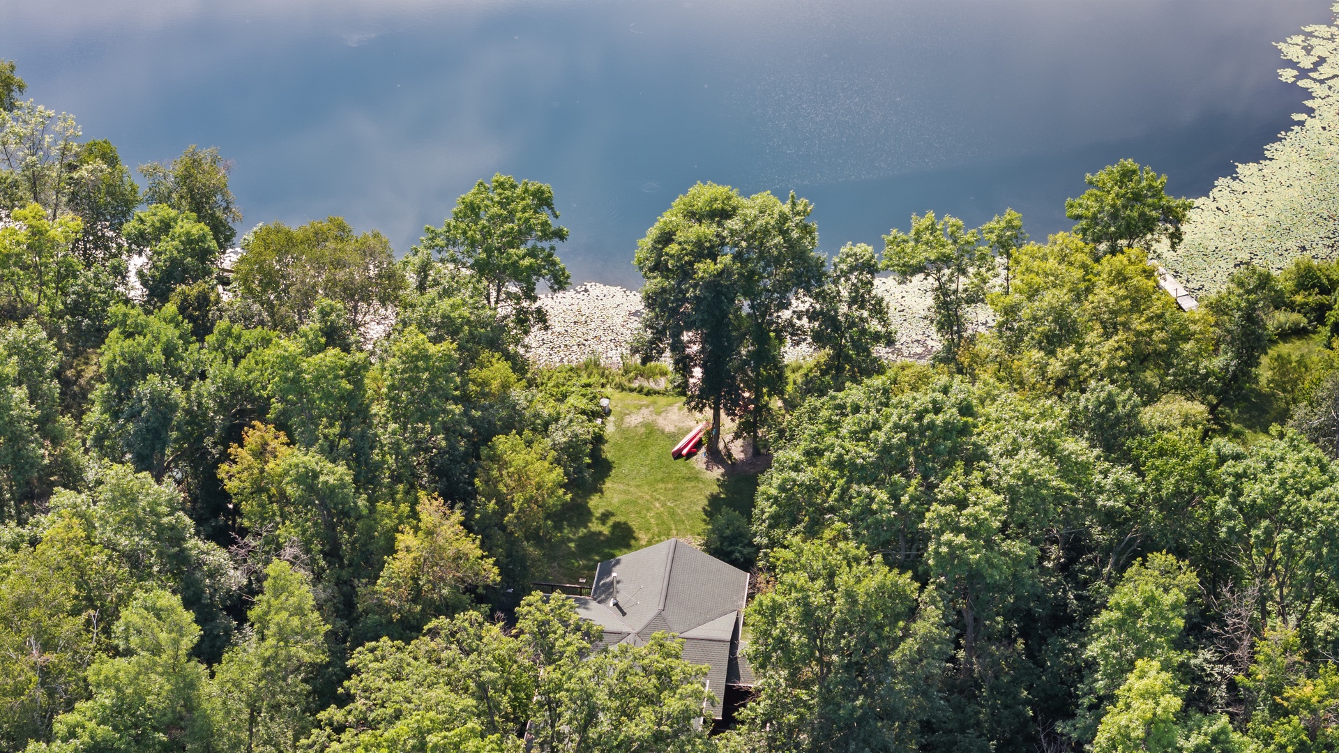 Aerial view of a secluded lakefront property nestled among mature trees with private shoreline access.