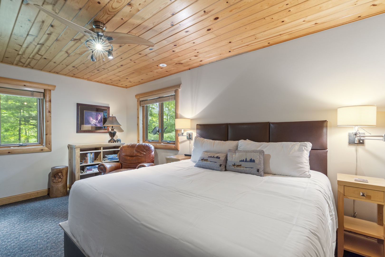 Relax beneath charming wood-paneled ceilings in your bright bedroom, where crisp linens and forest views through side windows create a peaceful mountain retreat.