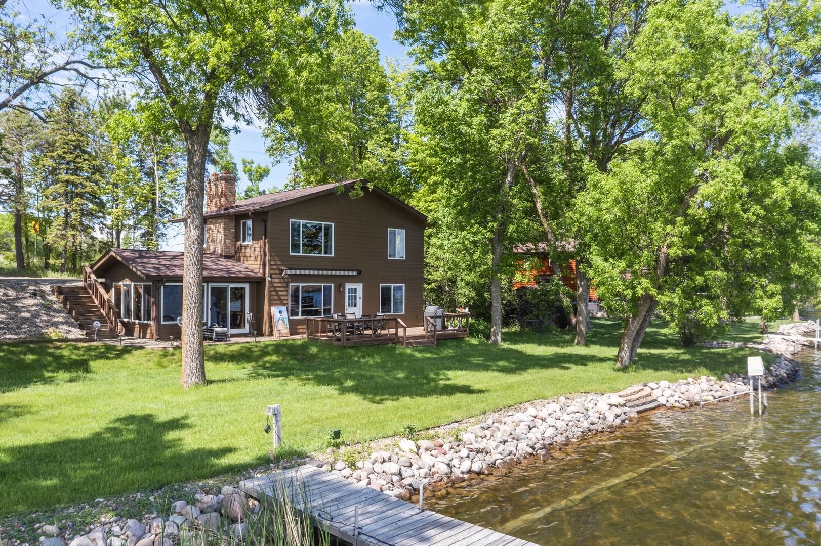 Charming two-story lakeside cabin nestled among towering trees with private dock and lush lawn—perfect for peaceful waterfront getaways.