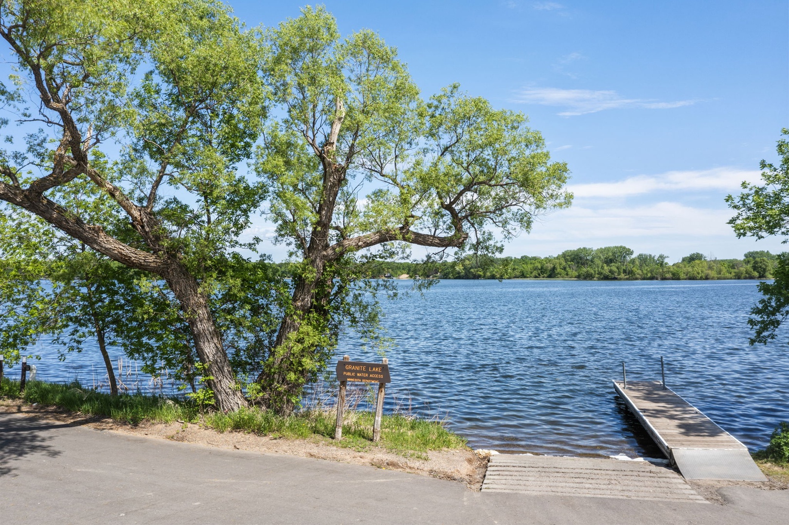 A serene lake with calm waters framed by mature trees, featuring a private dock and access point, offering scenic waterfront views in a peaceful natural setting.