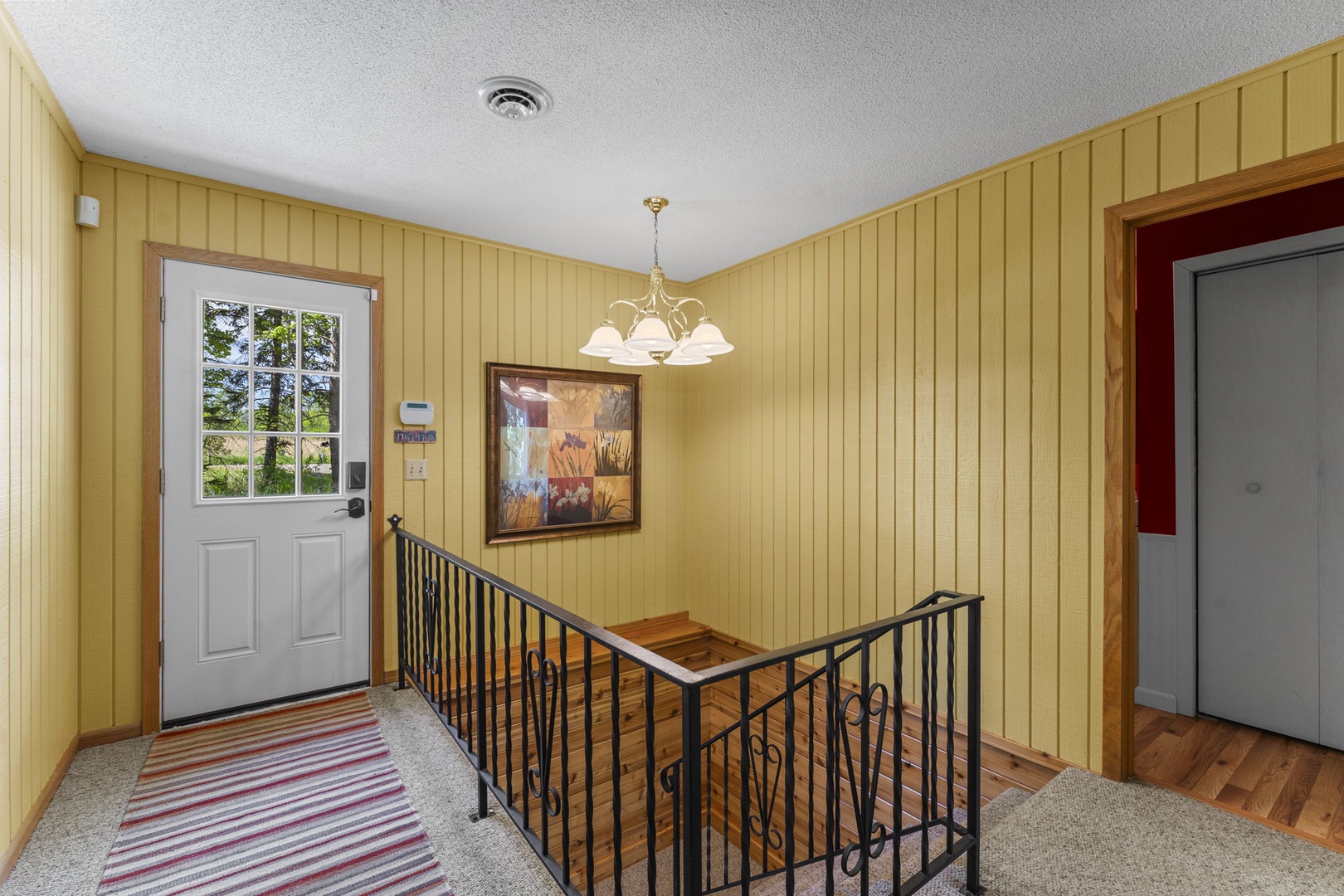 Entry space with bright yellow paneling, warm wood accents, and a welcoming chandelier. Natural light filters through the door, creating an inviting first impression as you arrive.