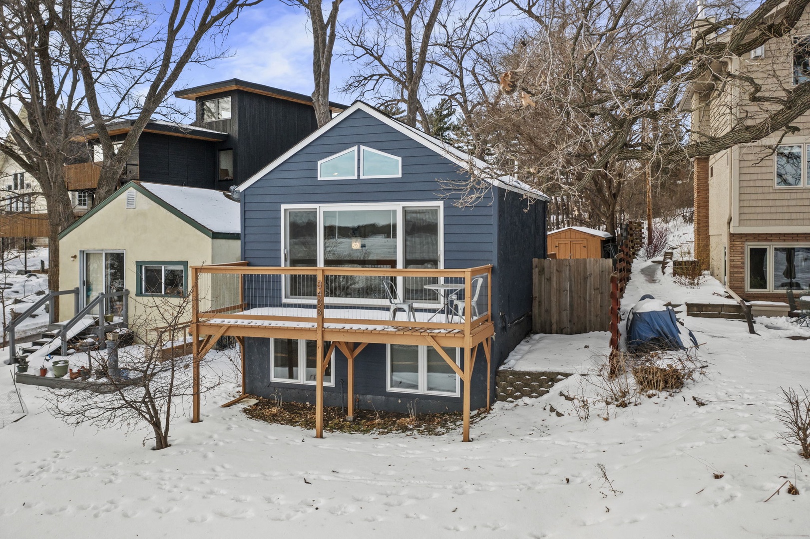 Charming blue cottage with wooden deck nestled in a quiet winter neighborhood, offering cozy retreat vibes.