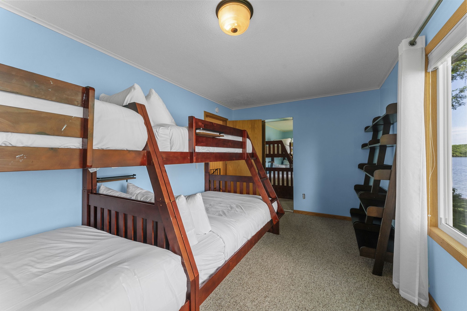 Rest easy in this spacious bunk room where everyone finds their perfect spot—fresh linens, peaceful blue walls, and water views through your window create a cozy retreat after adventure-filled days.