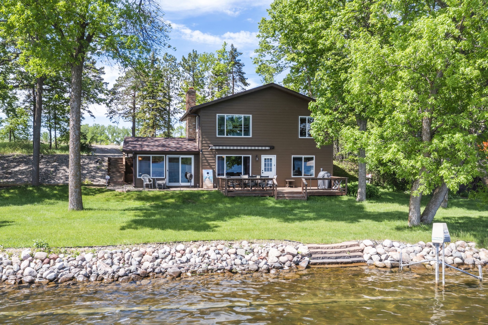 Spacious lakefront property nestled among mature trees with private waterfront access and expansive lawn for outdoor activities. Direct beach access via stone retaining wall and dock.