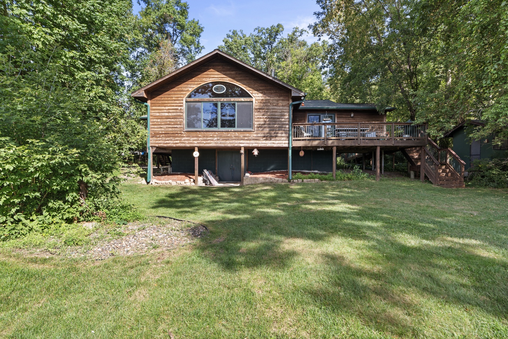 A charming cedar-sided retreat set among mature trees on a spacious lawn, offering a peaceful wooded escape with a welcoming wrap-around deck and elevated design.