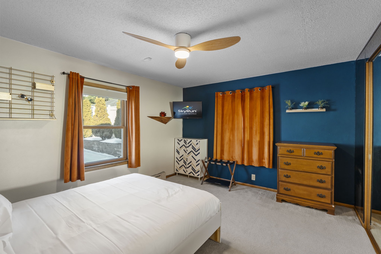 Unwind in your stylish bedroom with warm wood accents and vibrant blue walls. The ceiling fan keeps you cool while smart TV entertainment awaits.