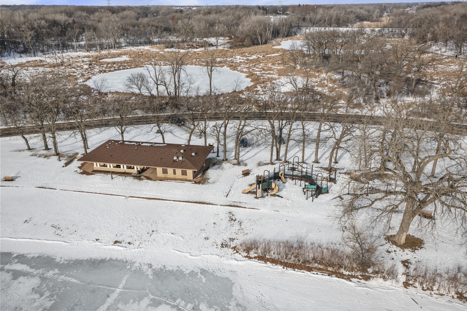 Aerial view of the property showcasing a winter wonderland with snow-covered grounds, playground facilities, and peaceful natural surroundings.