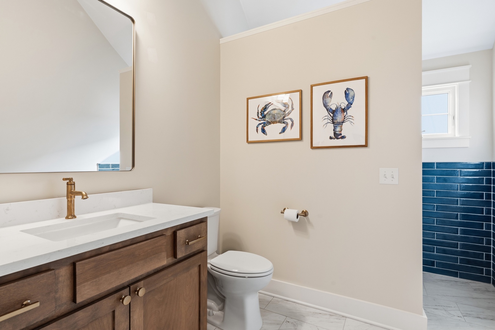 Freshen up in your charming coastal bathroom featuring warm wood cabinetry, a gleaming white vanity, and playful seaside artwork that sets a relaxed beach-house tone.