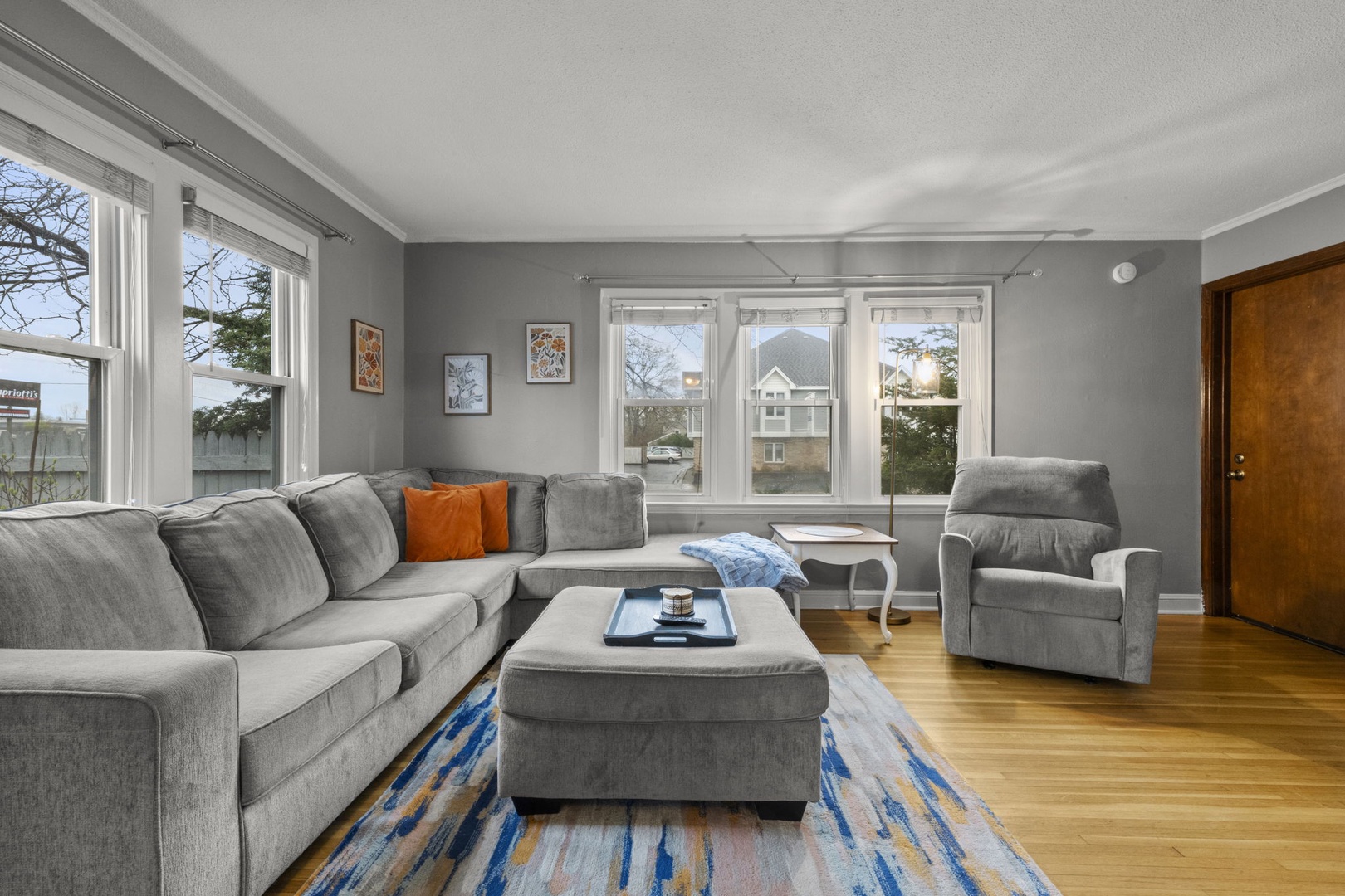 Sink into the plush sectional and let natural light fill your living space. Large windows frame neighborhood views while warm hardwood floors create a cozy, inviting atmosphere for relaxation.