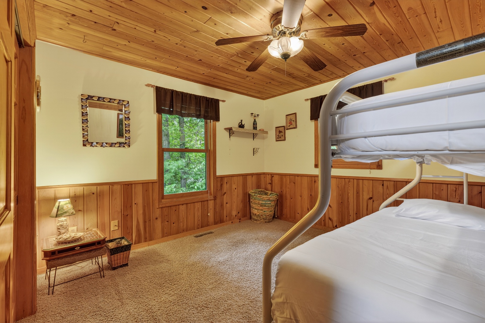 Cozy bunk room with rustic wood paneling, ceiling fan, and a window looking out to leafy green views—perfect for family or friends sharing the adventure.