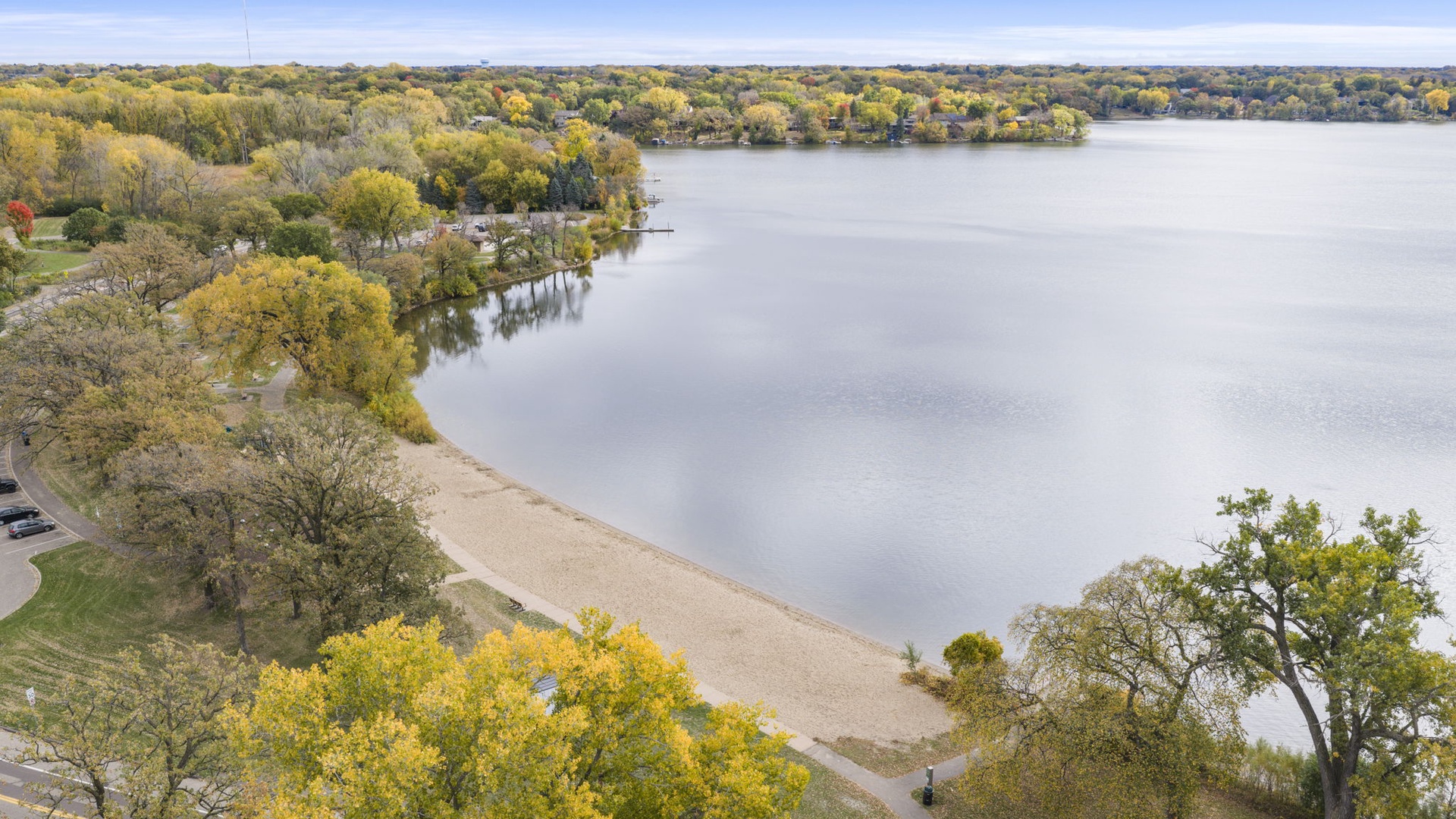 Aerial view of the park's beach, surrounded by autumn foliage and a peaceful sandy beach area along the water's edge.