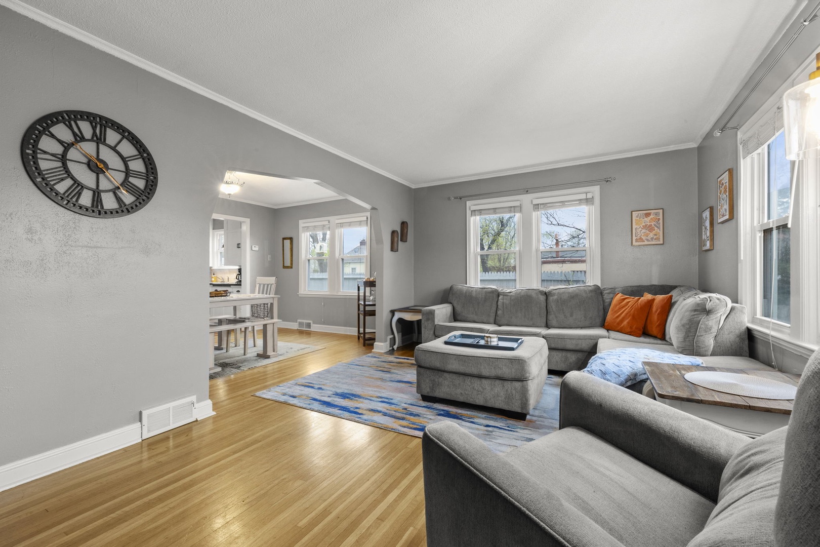 Settle into this bright, inviting living room with plush sectional seating, gleaming hardwood floors, and large windows that fill the space with natural light—perfect for your downtime.