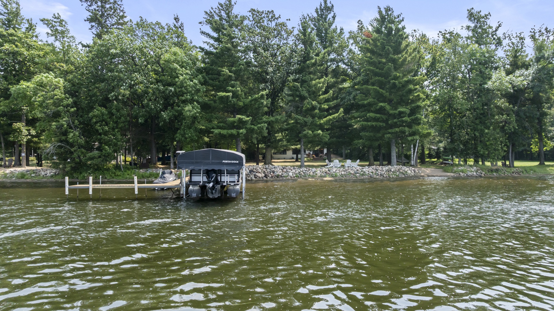 A private boat dock sits nestled among tall pines and mature trees along the pristine lakeshore, offering direct water access and surrounded by peaceful natural beauty.
