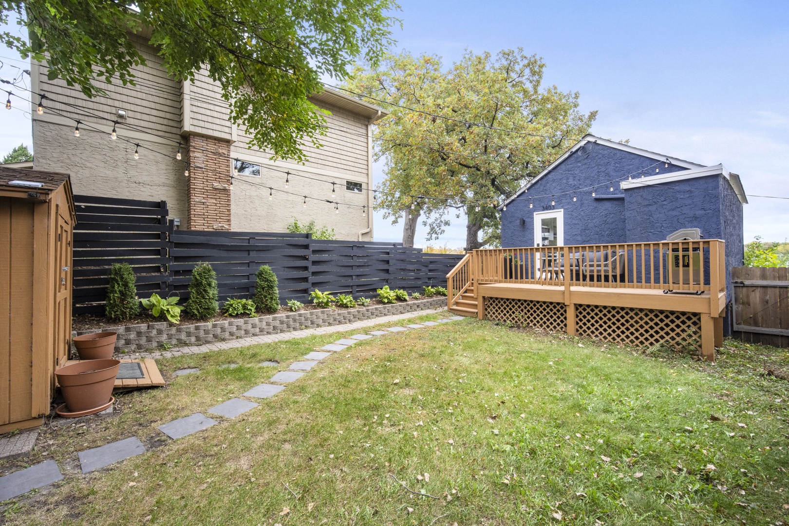 Quiet residential backyard featuring a landscaped lawn, wooden deck, and mature shade trees in a peaceful neighborhood setting.