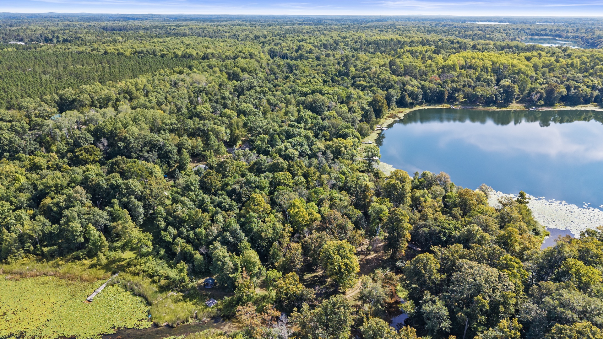 An aerial view reveals dense forest surrounding a tranquil lake, offering a peaceful natural setting for the property.
