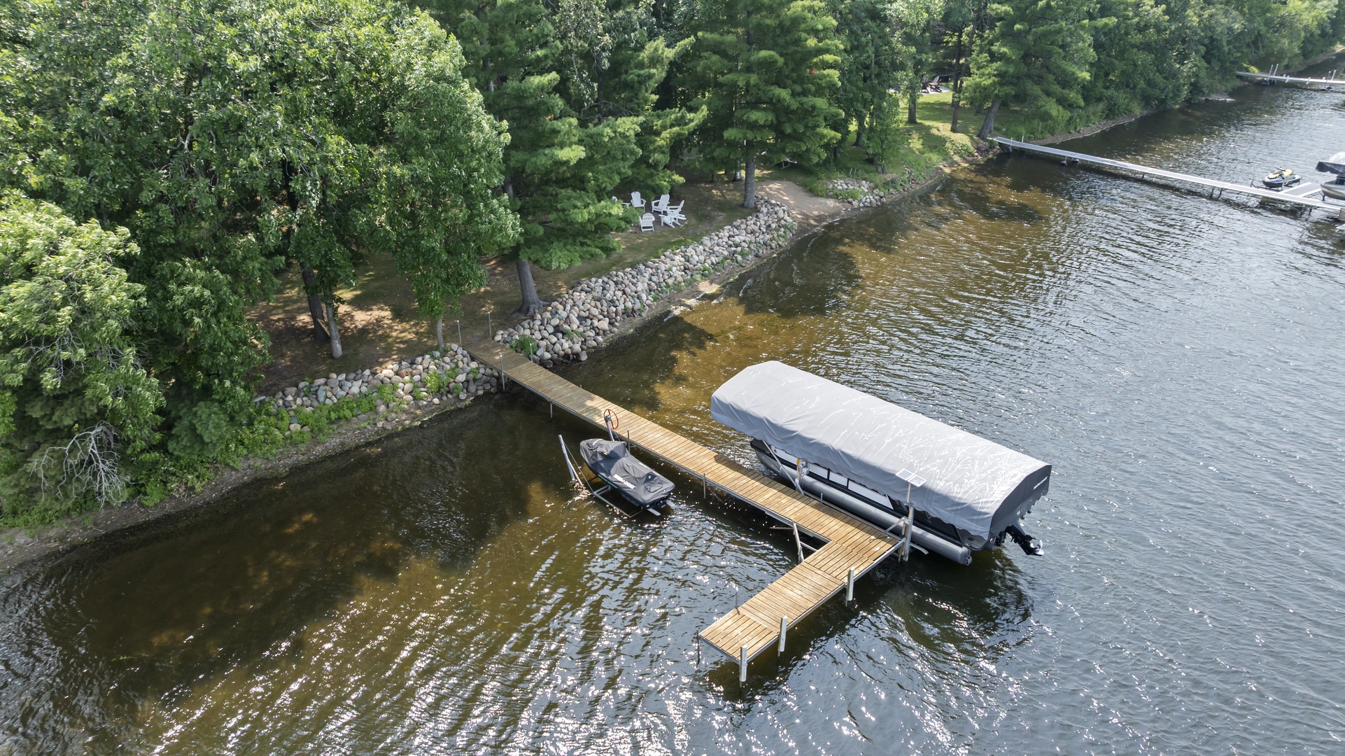 Aerial perspective of a secluded lakefront property featuring a private dock with two boat slips surrounded by lush forest and a tranquil shoreline, perfect for waterfront relaxation and outdoor recreation.