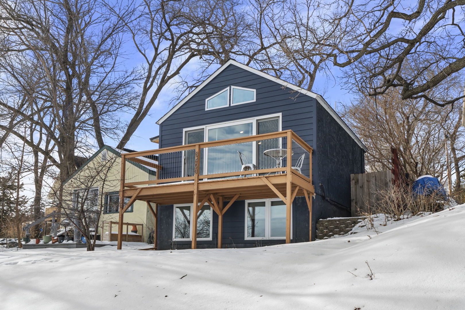 Modern lakeside retreat with spacious deck and large windows nestled among mature trees in a peaceful winter setting.