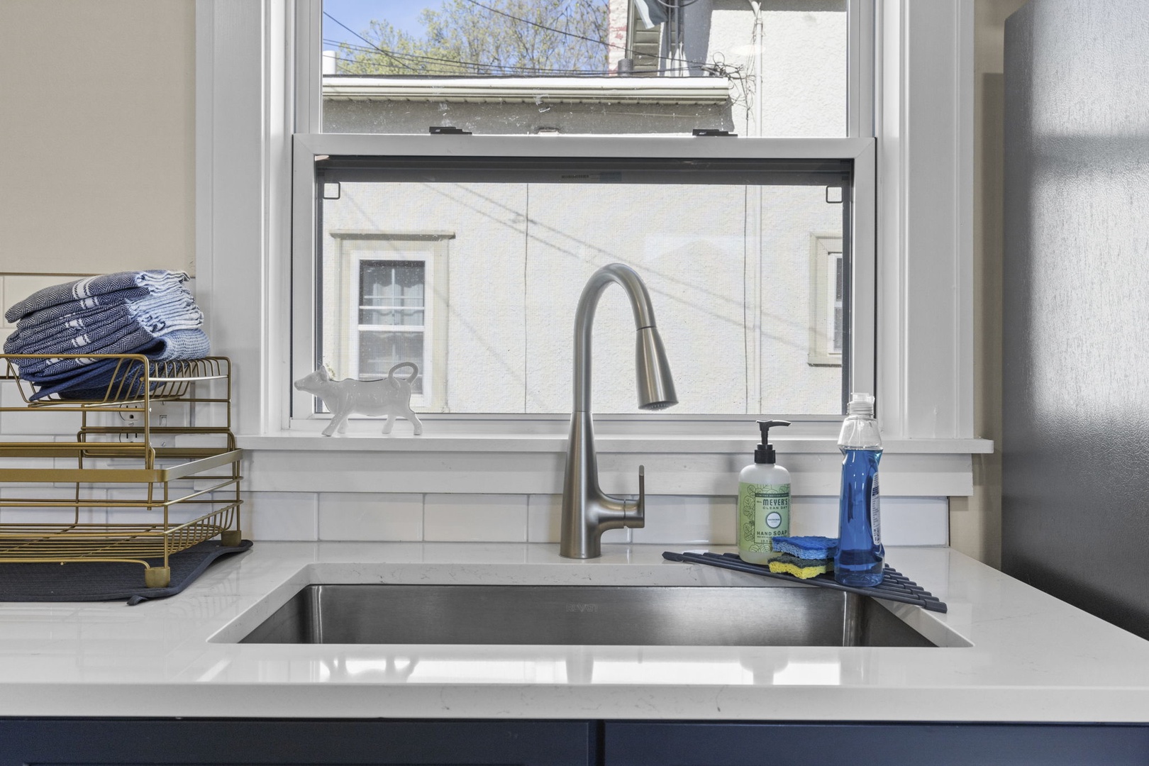 Kitchen sink detail with deep stainless basin, pull-down faucet, quartz countertops, and classic subway tile backsplash — clean, bright, and functional.