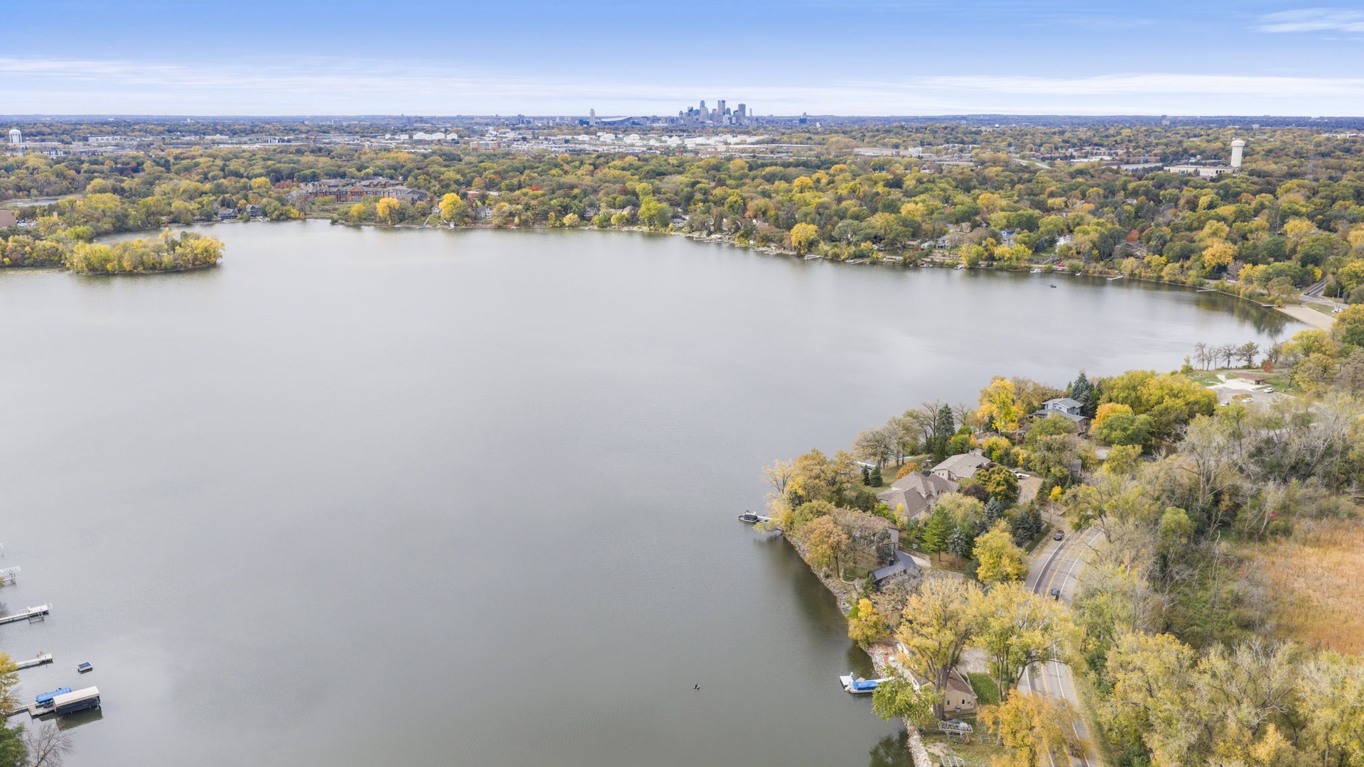 Nestled along a serene lake surrounded by autumn foliage, this property offers peaceful waterfront living with a distant city skyline on the horizon.