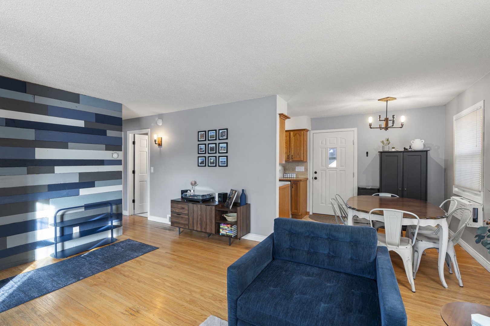 Relax in your stylish open-plan living space with rich hardwood floors, modern blue sofa, and a striking geometric accent wall.