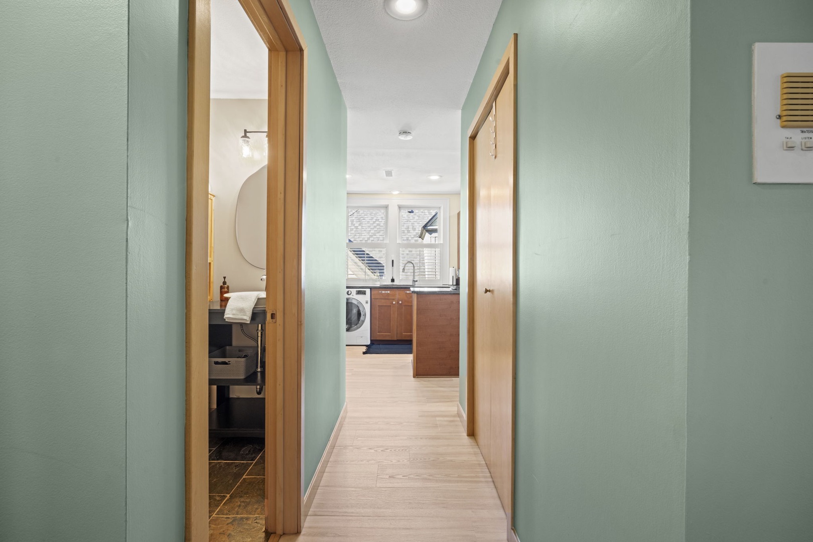 A bright, well-organized hallway connects your bathroom and fully equipped kitchen, making it easy to move through your home. Light wood flooring and calming blue-green walls create a fresh, welcoming feel throughout.