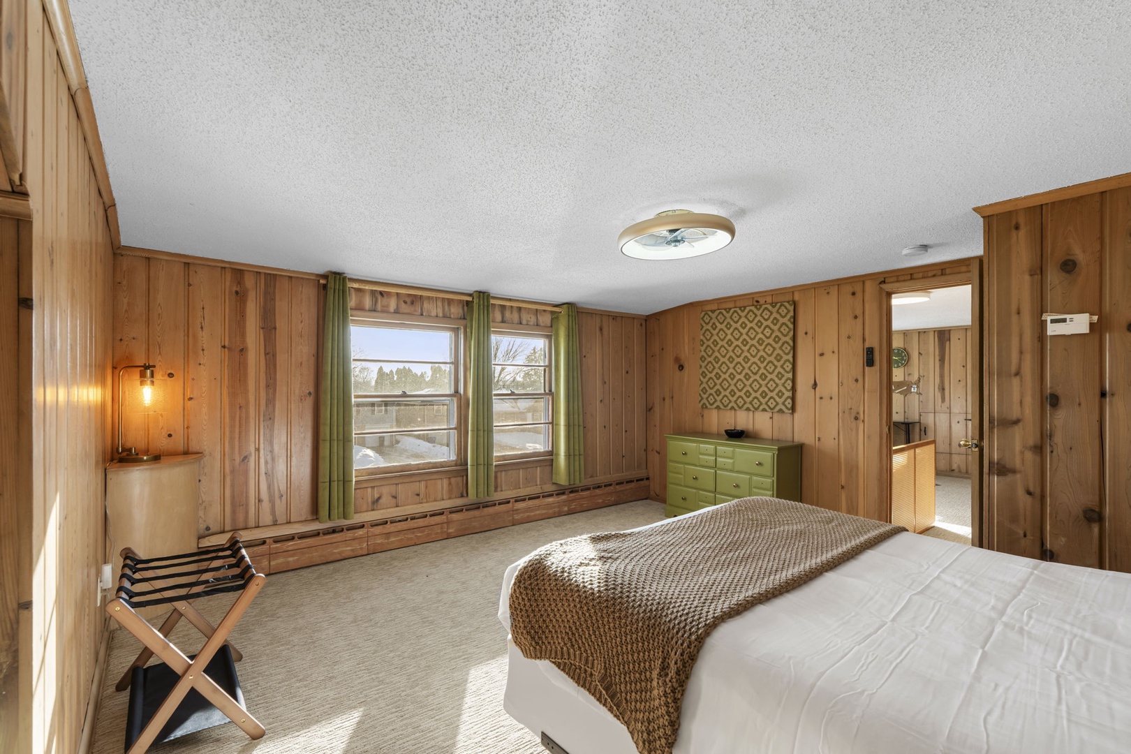 Relax in your cozy wood-paneled bedroom featuring warm natural textures and bright windows.