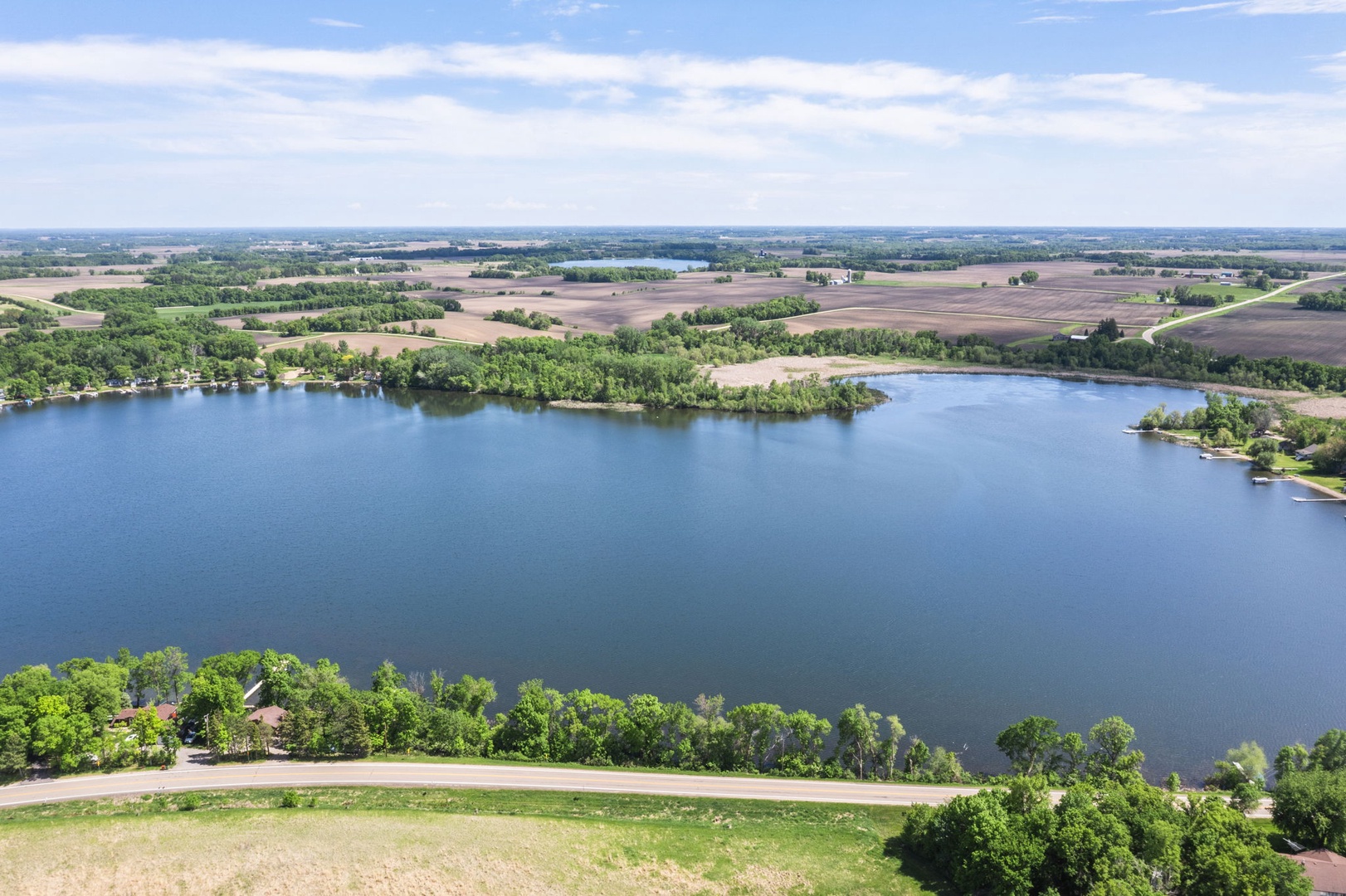 Aerial view of a serene lakeside location, surrounded by lush greenery, farmland, and open skies—a peaceful rural setting near the property.