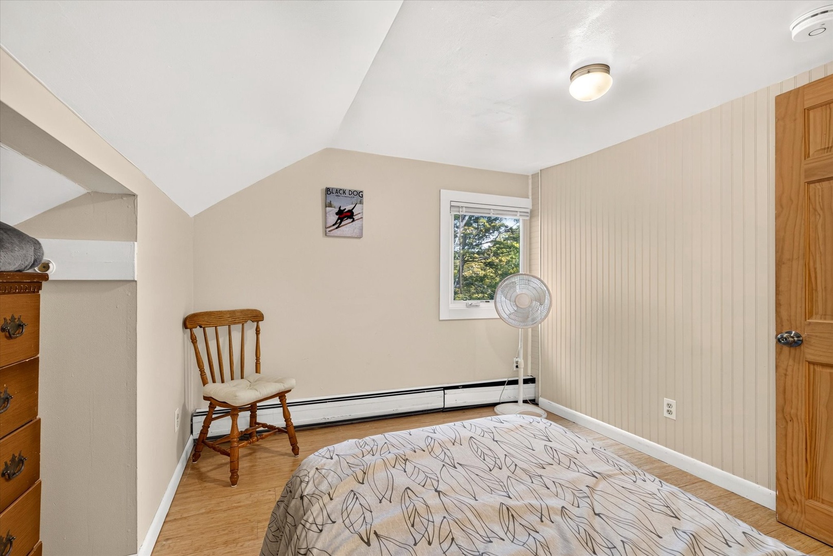 Curl up in this bright, peaceful bedroom with charming beadboard walls and a view of leafy greenery just outside your window.