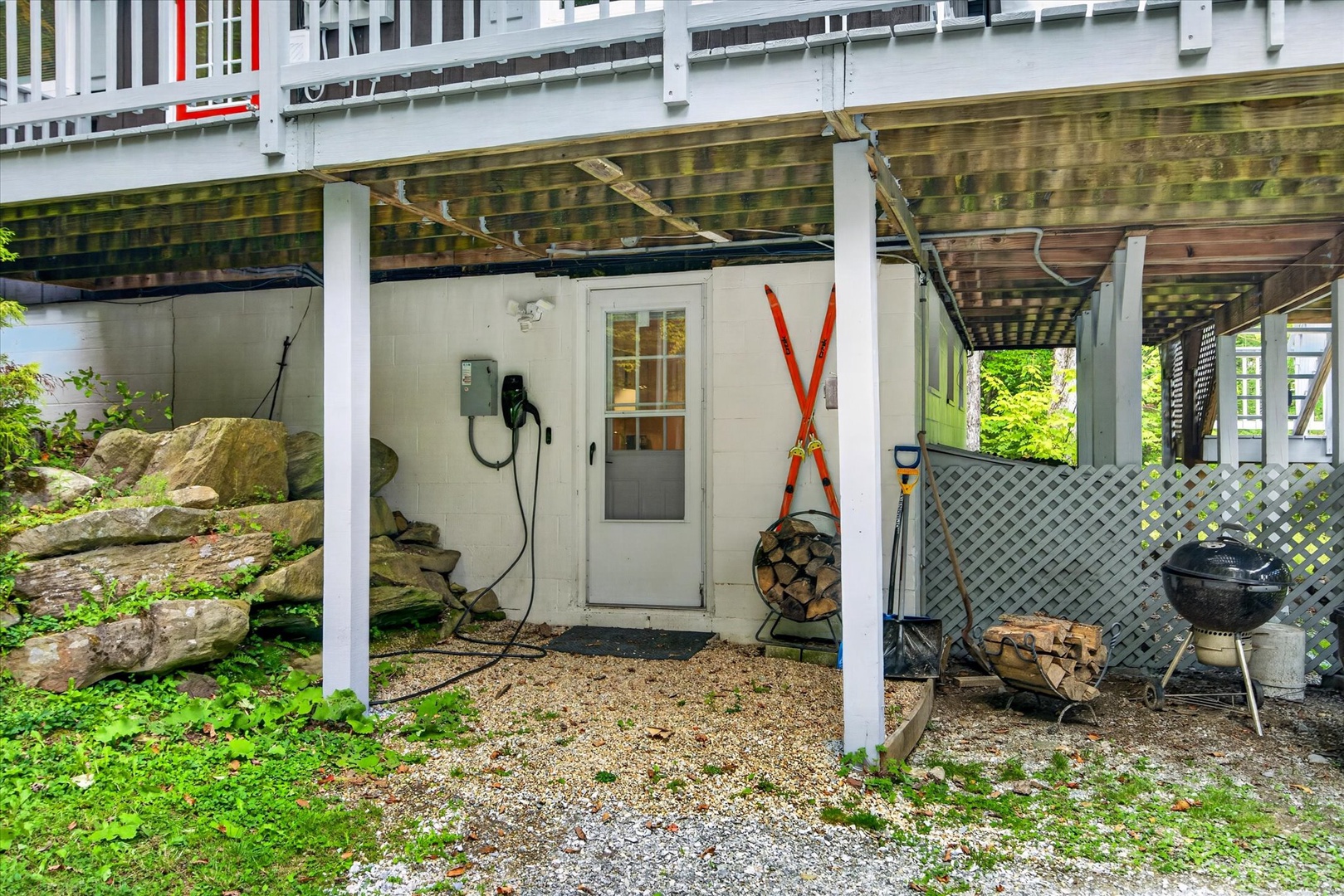 The property features a covered outdoor area beneath the deck, providing a sheltered space with natural stone accents and lattice fencing for added privacy.