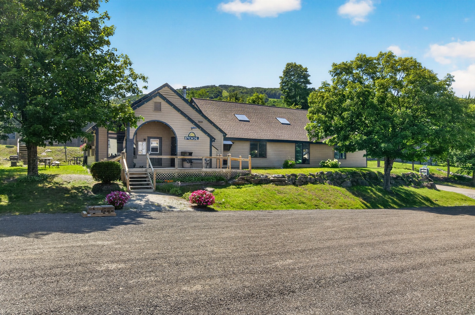 The property sits nestled among mature trees and lush lawns, offering a peaceful retreat with mountain views in the background and ample parking for guests.