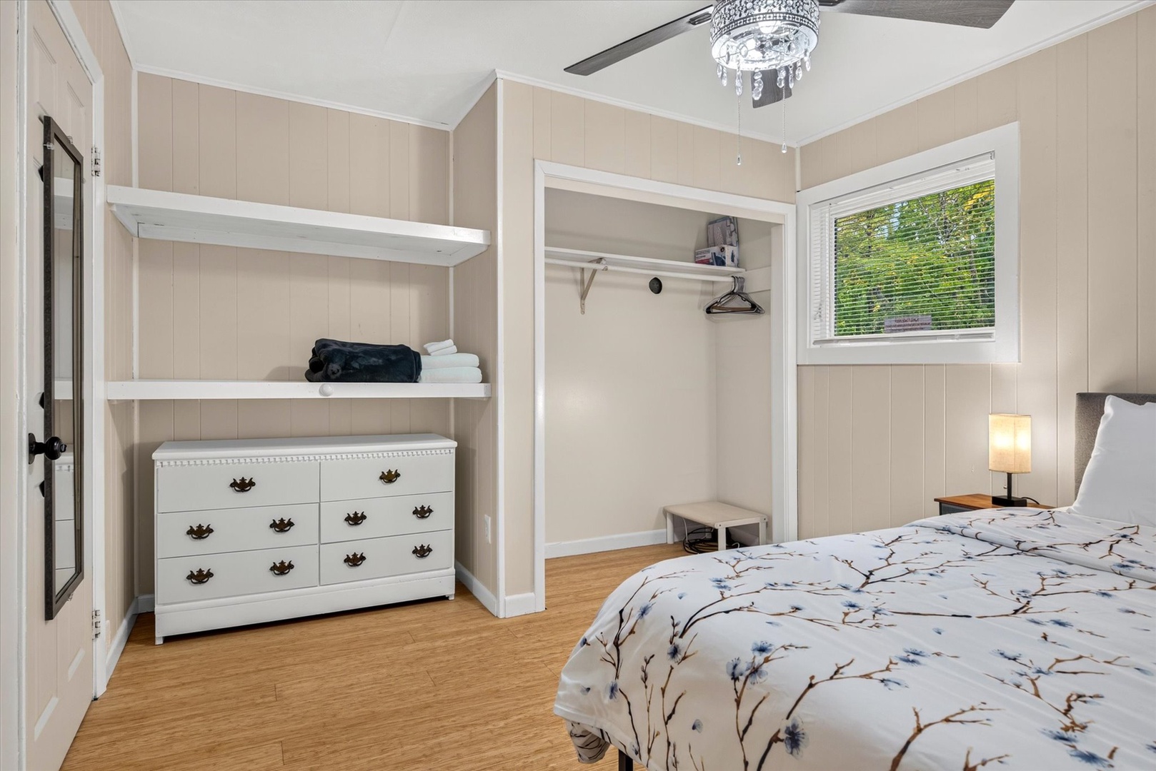 Your peaceful bedroom features a cozy bed, plenty of storage with open shelving and a dresser, and a ceiling fan to keep you comfortable. Natural light from the window brightens your restful retreat.