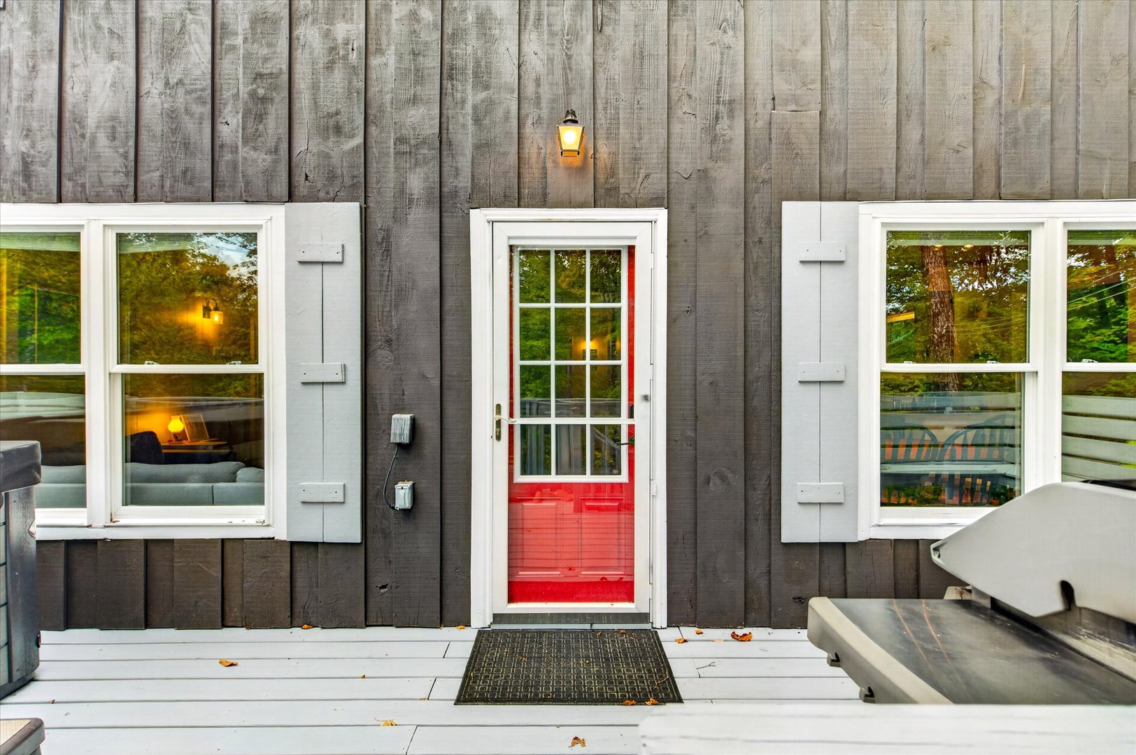 This charming exterior features a rustic wood facade with a welcoming red door and white shutters. The property offers a peaceful retreat surrounded by nature.