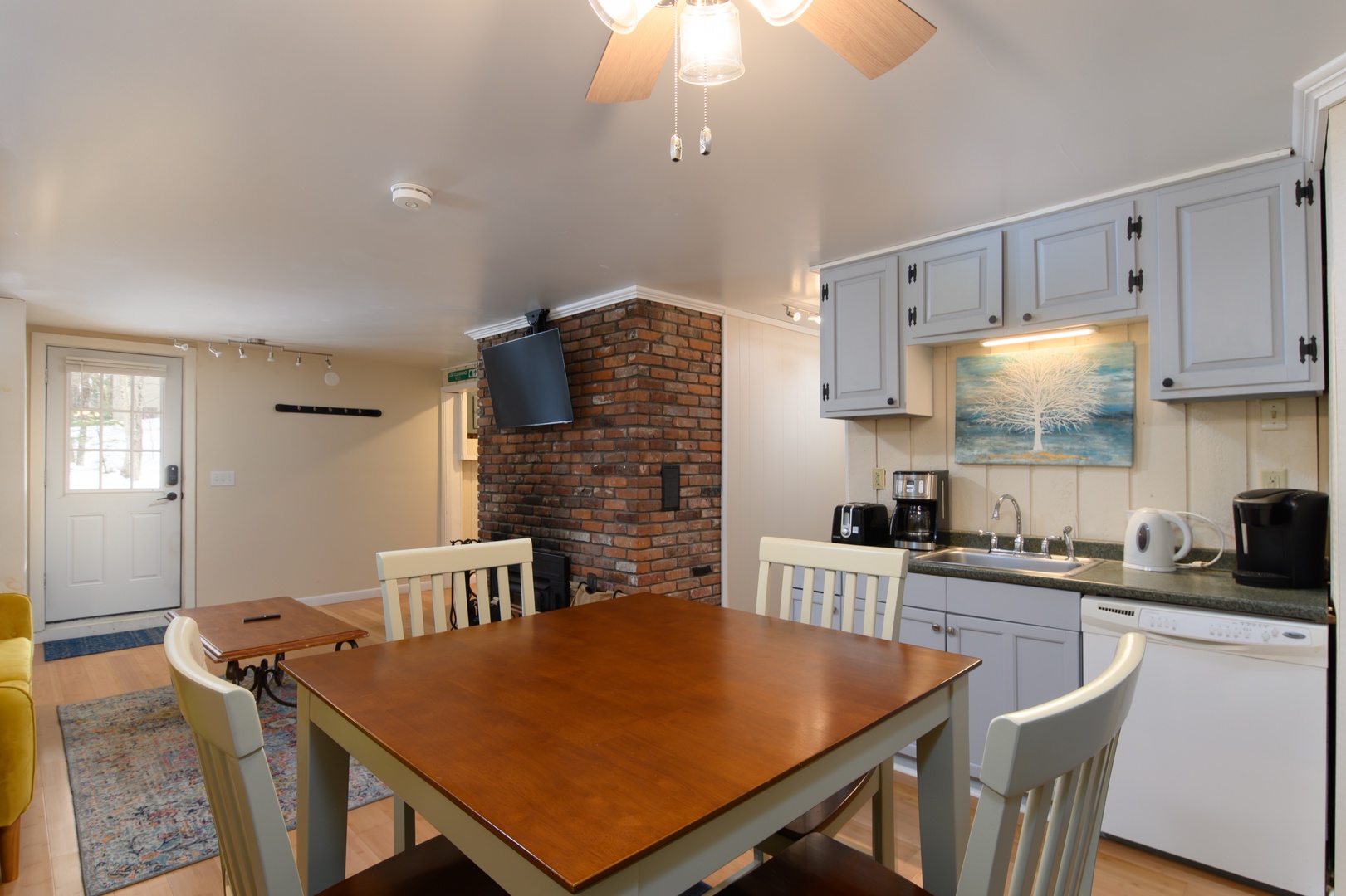 Your cozy kitchen awaits with modern appliances, warm brick fireplace, and inviting dining table perfect for morning coffee or evening meals together.