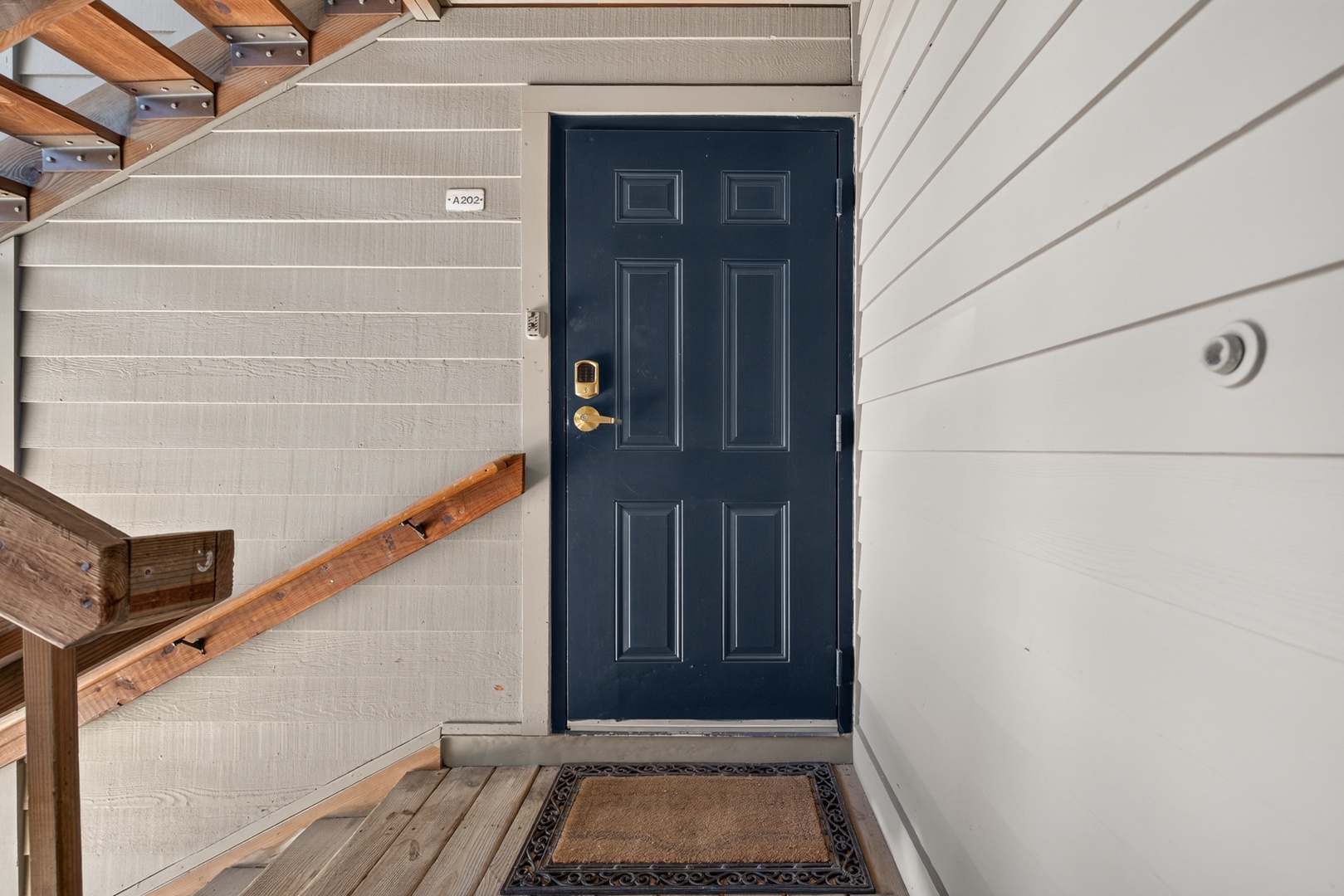 Your private entrance awaits behind a classic navy door, with wooden stairs leading up to your coastal retreat.