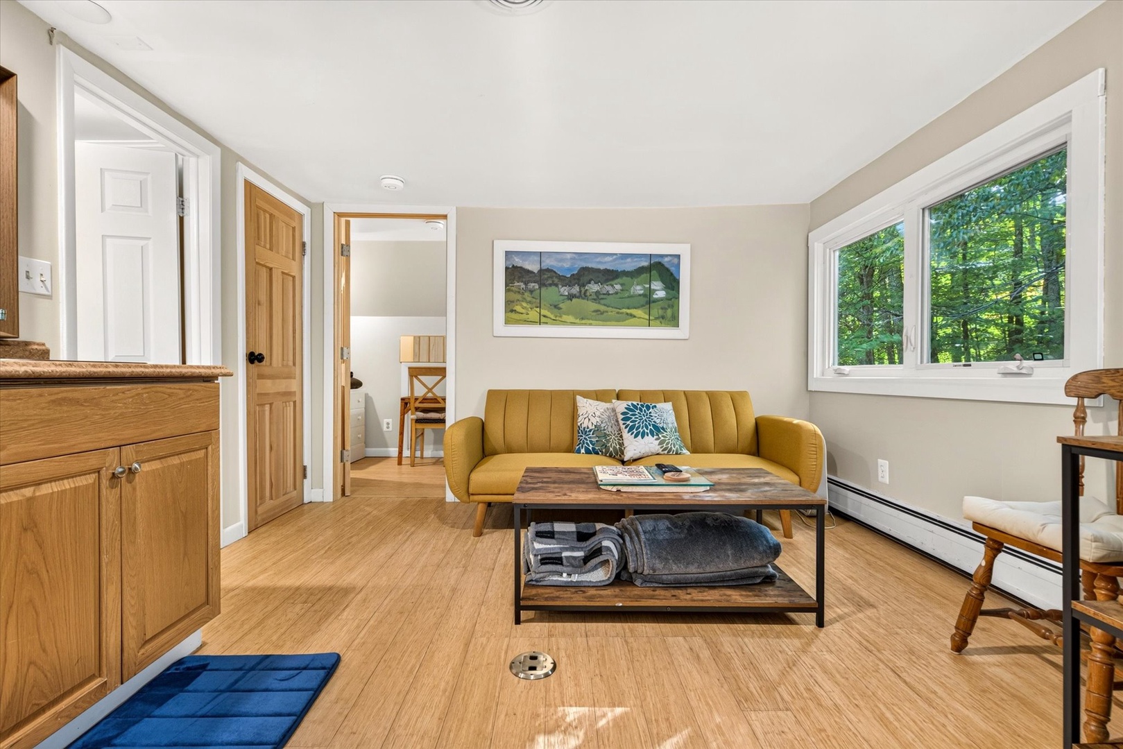Relax in your bright living space with a comfortable sofa, warm wood floors, and large windows framing views of the peaceful forest beyond.