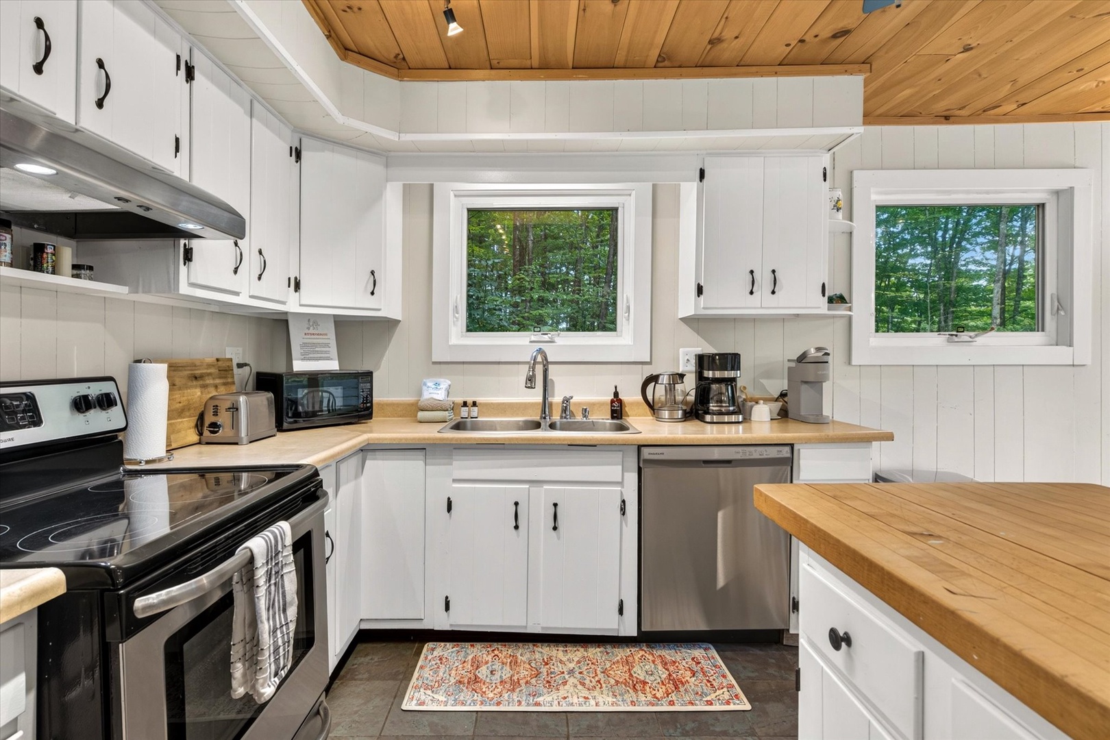 Your fully equipped kitchen features warm wood countertops, crisp white cabinetry, and peaceful forest views through the windows—perfect for your morning coffee as you plan the day's adventures.