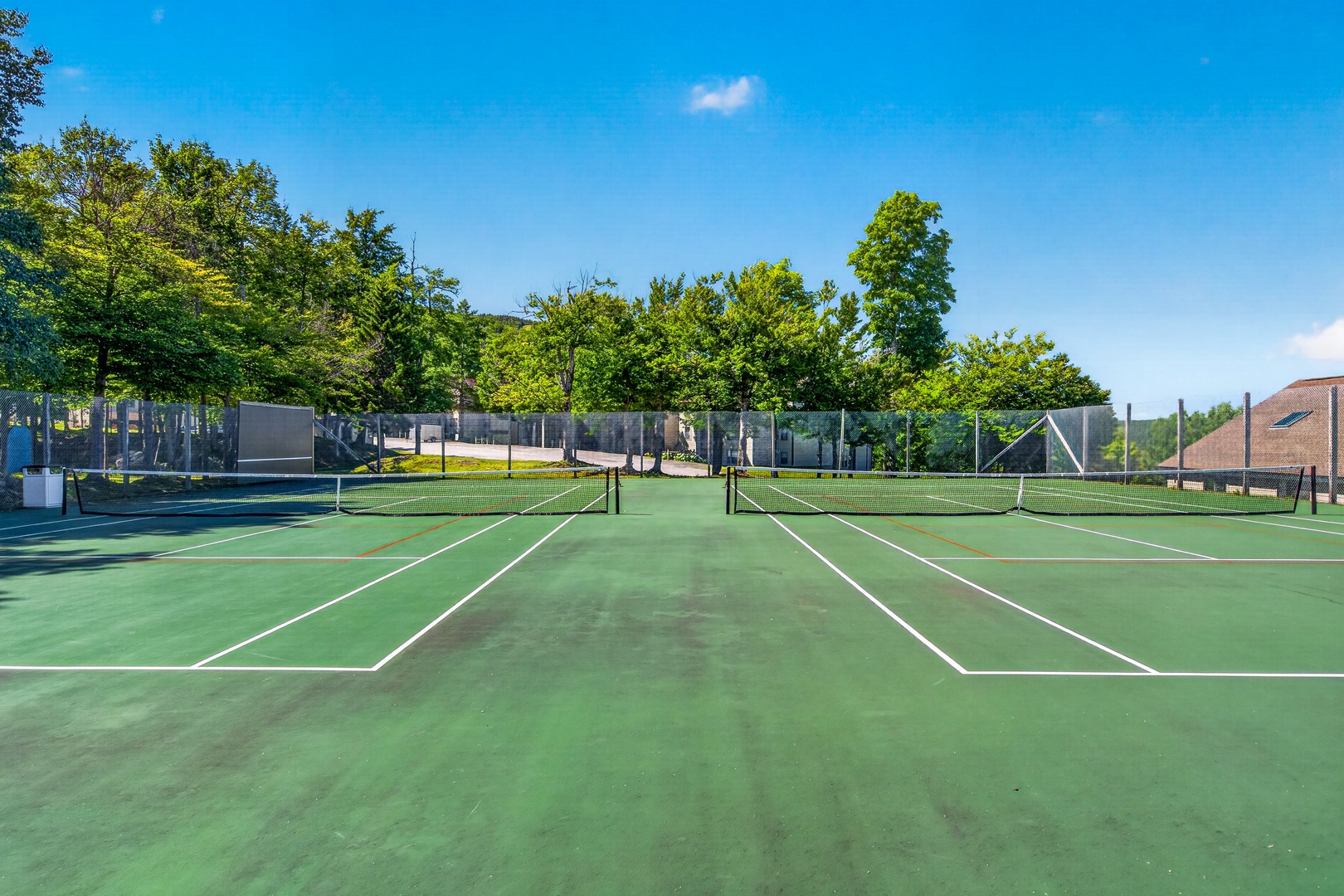 A private tennis court with pristine green surface awaits your friendly match, surrounded by lush trees and sunny skies that complete your ideal outdoor escape.