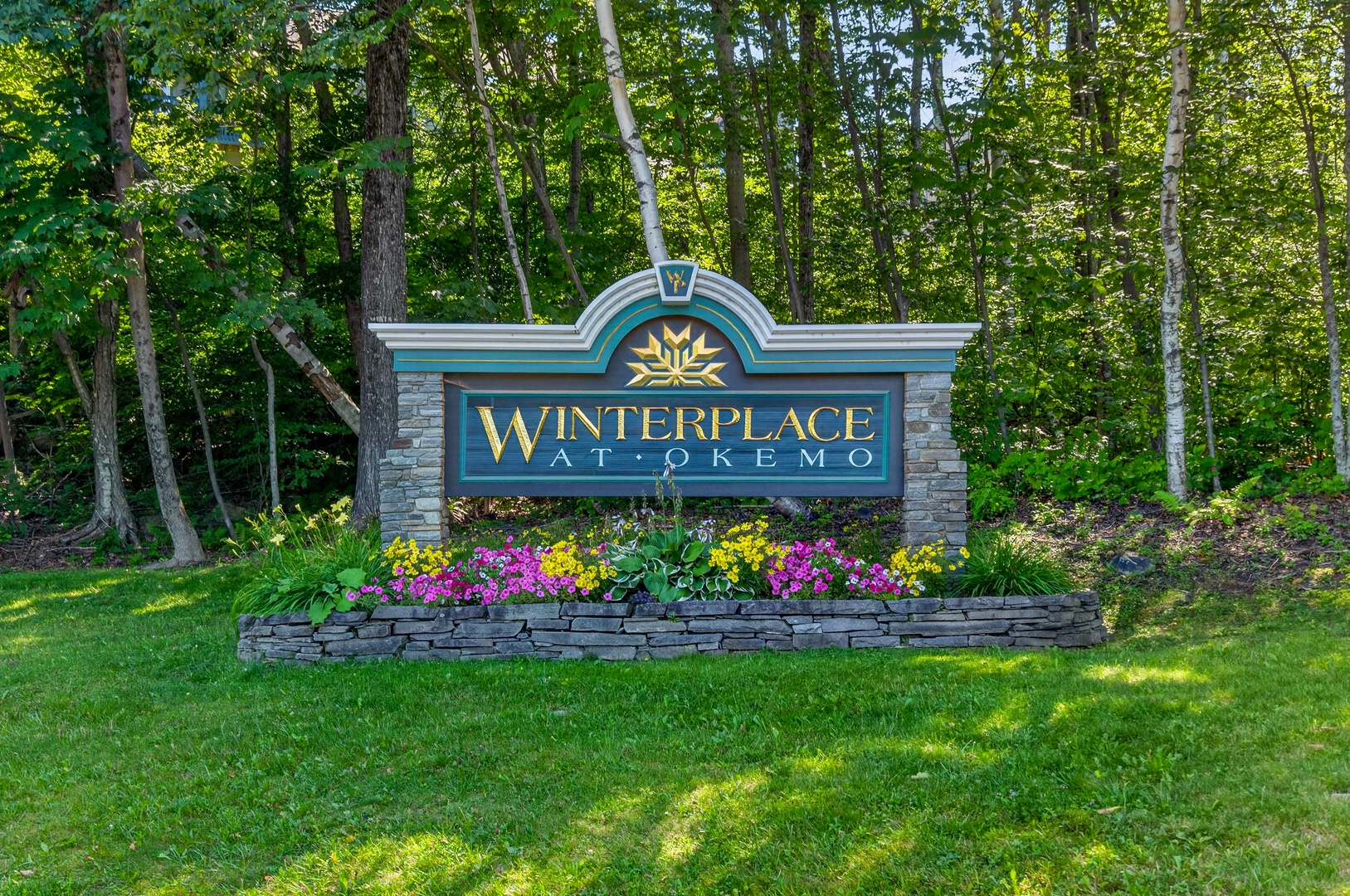 The entrance marker at Winterplace at Okemo welcomes visitors to a wooded mountain setting surrounded by lush summer foliage.