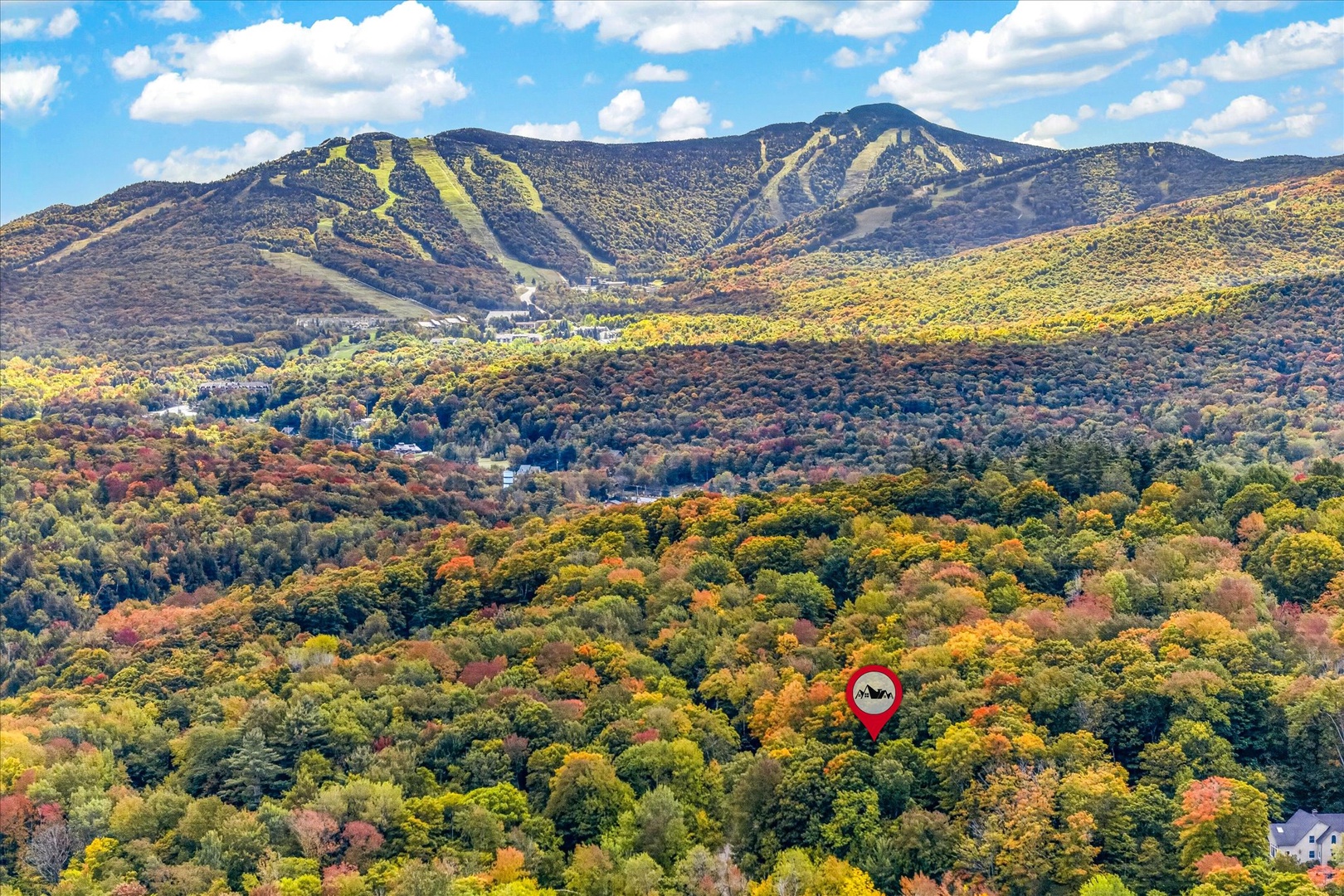 Aerial view of a property nestled among vibrant autumn foliage with mountain ski slopes rising in the distance.