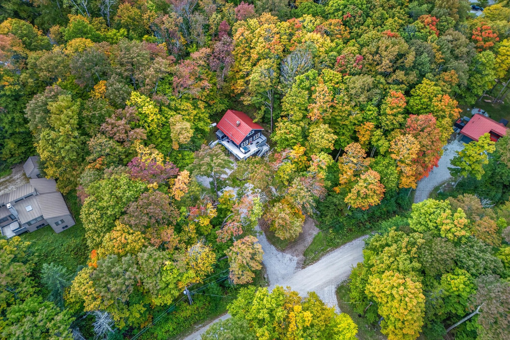 Aerial view of a charming property nestled among vibrant autumn foliage, with seasonal colors painting the landscape in gold, orange, and red tones.