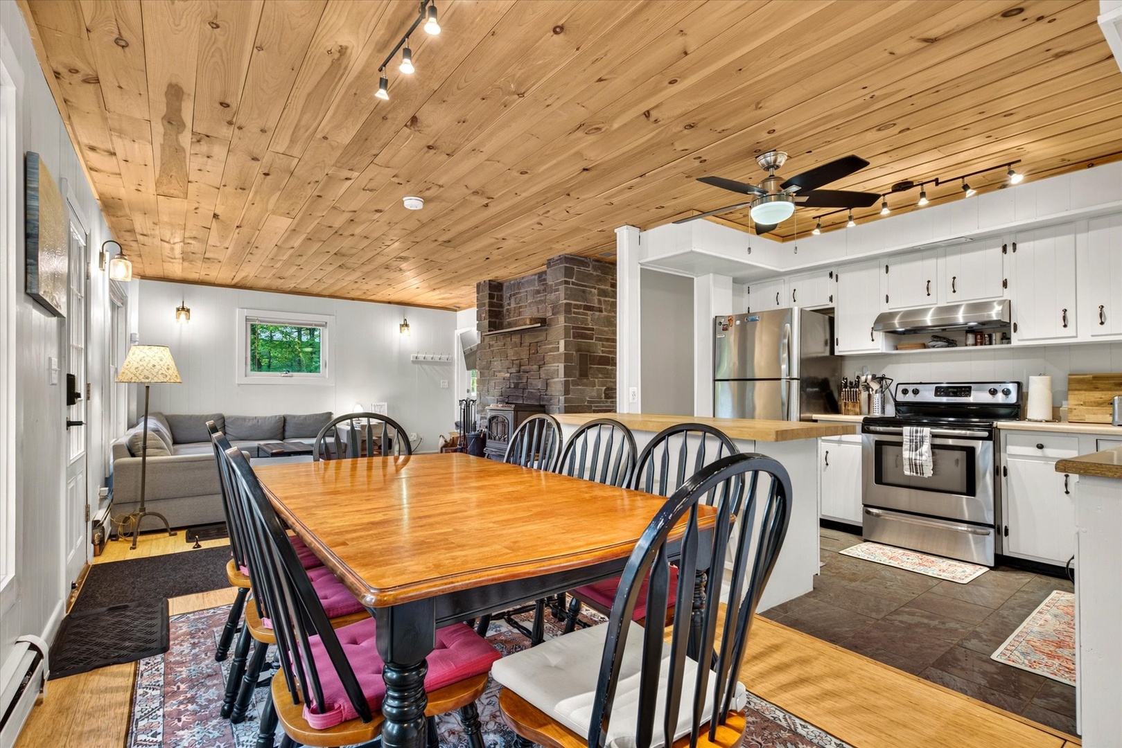 Gather around the large farmhouse table beneath warm wood ceilings and enjoy meals together, with the fully equipped kitchen just steps away and a cozy living area inviting relaxation by the fireplace.