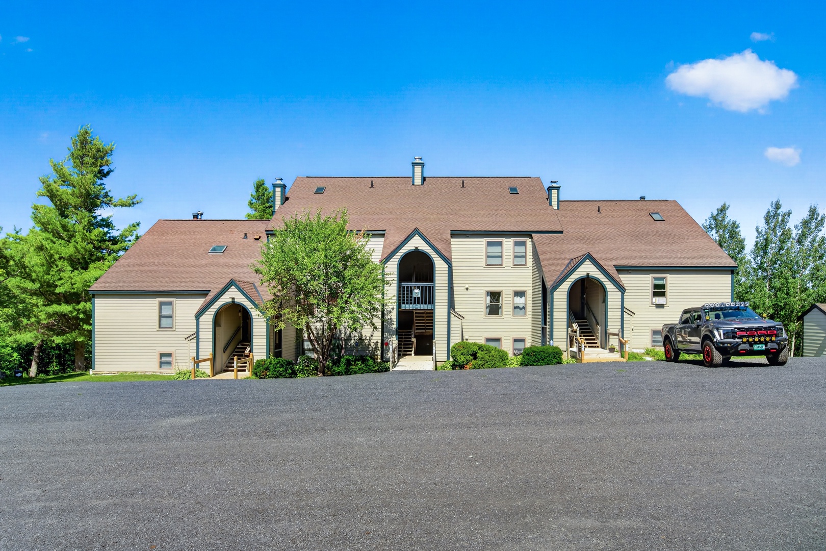 The property features a multi-level building with arched entryways, set against a backdrop of lush greenery and clear blue skies, with convenient on-site parking for guests.