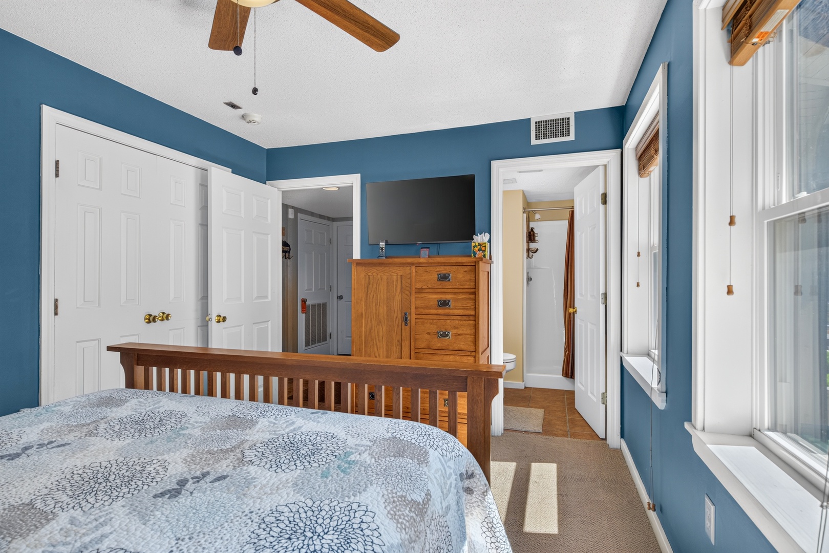 Slip into your peaceful retreat with calming blue walls, warm wooden furniture, and a ceiling fan to keep you comfortable. Natural light fills your space, and multiple doors lead to your own private bathroom and storage.