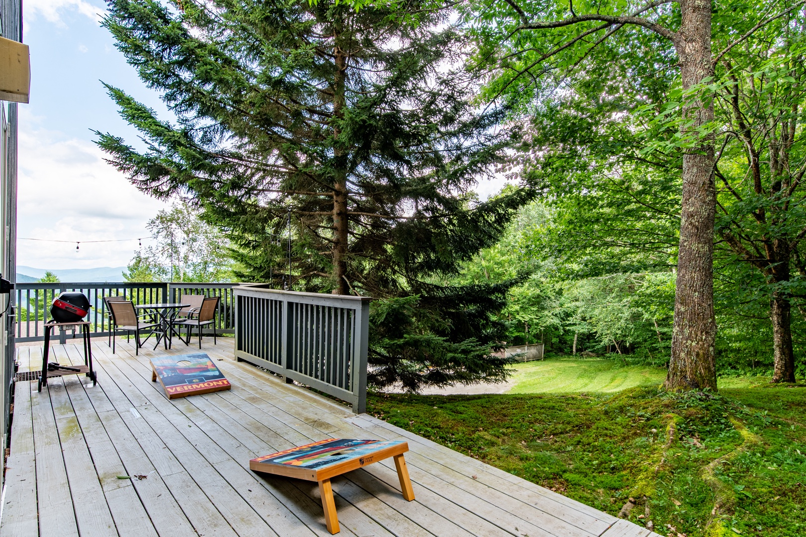 Spacious deck with cornhole games overlooks lush evergreens and lawn—perfect for your morning coffee or evening barbecues surrounded by nature.