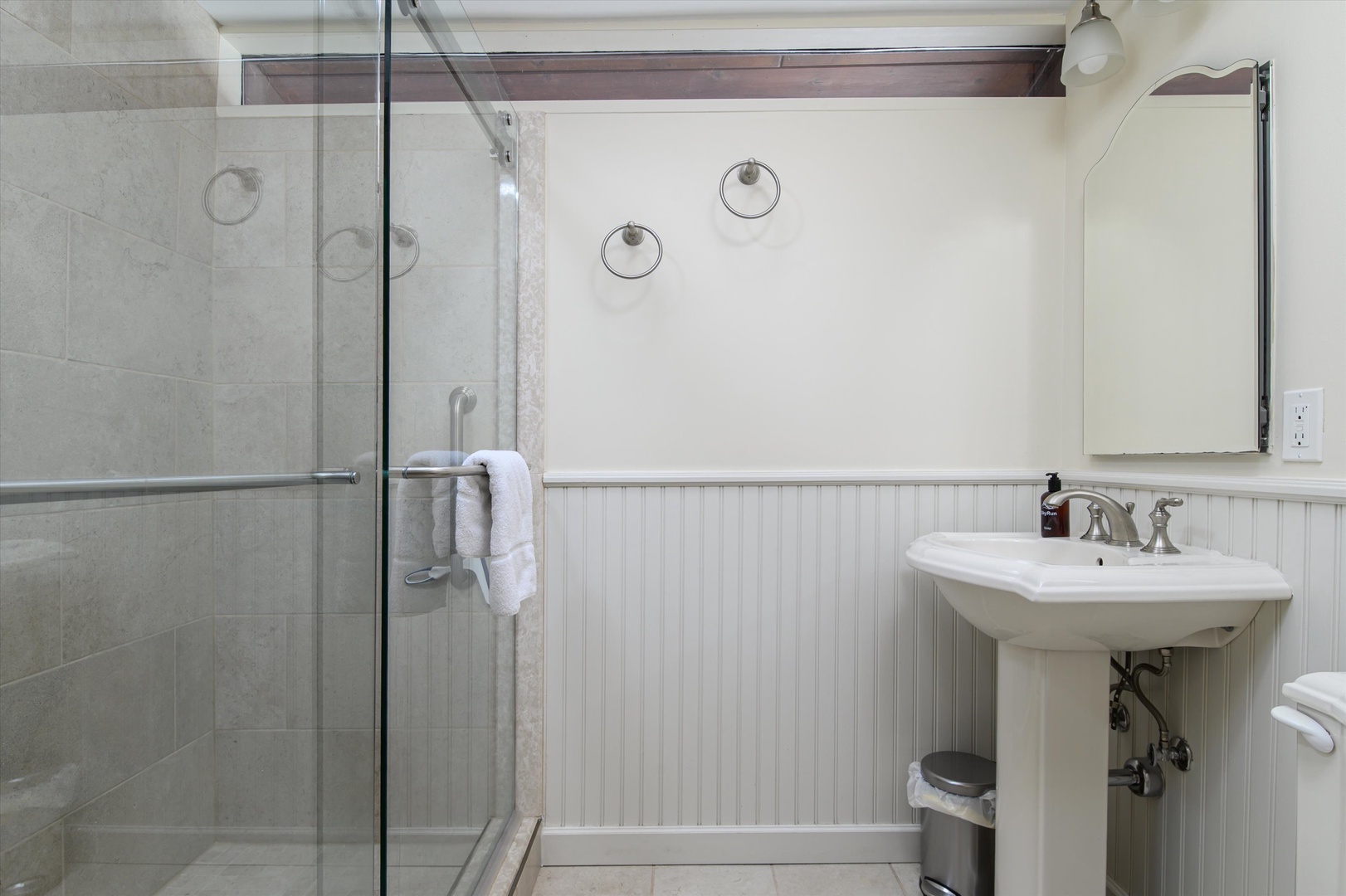 Step into your spa-like main level bathroom with a spacious glass shower and elegant pedestal sink, where fresh towels await your arrival.